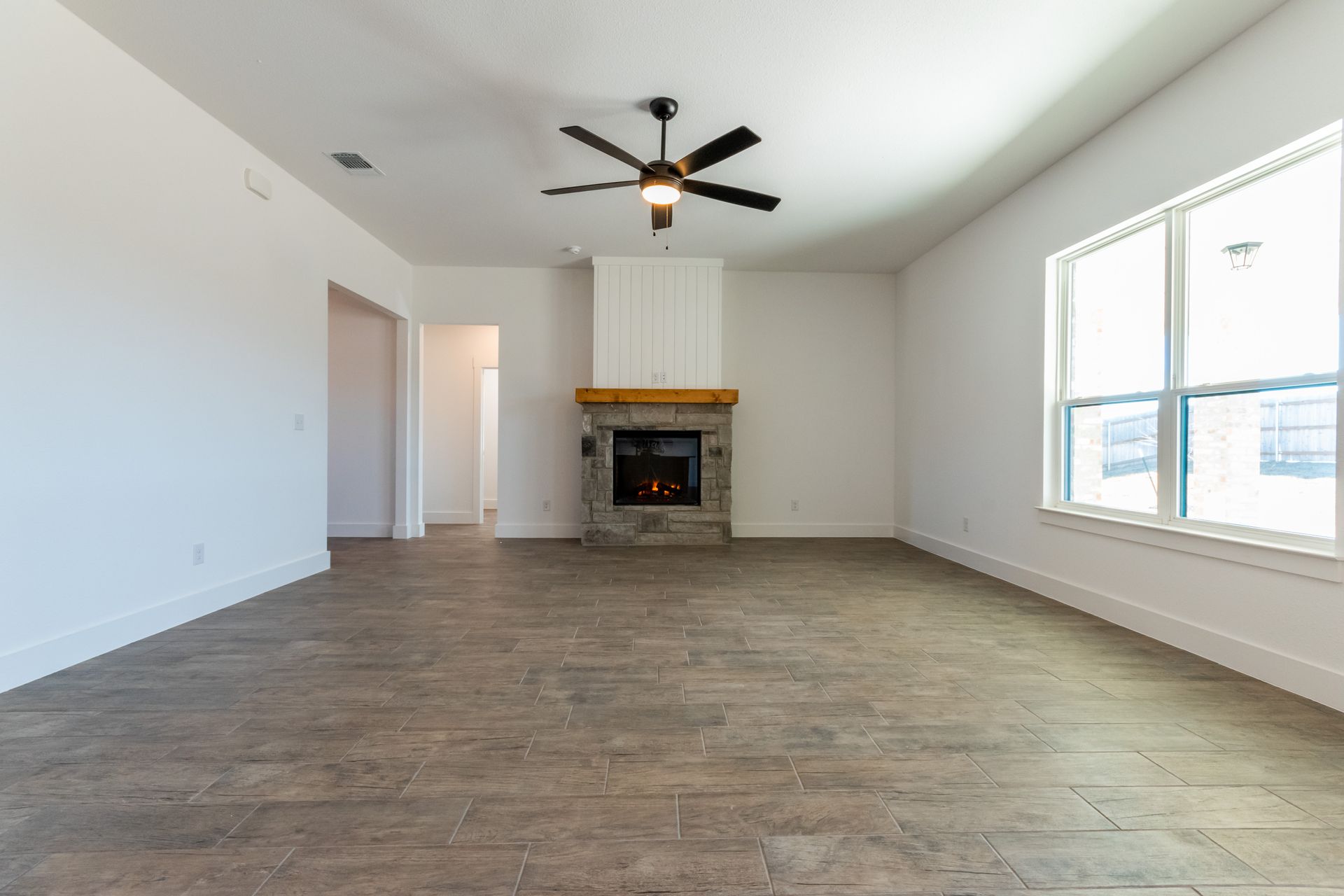 Empty living room with fireplace, ceiling fan, and large window.