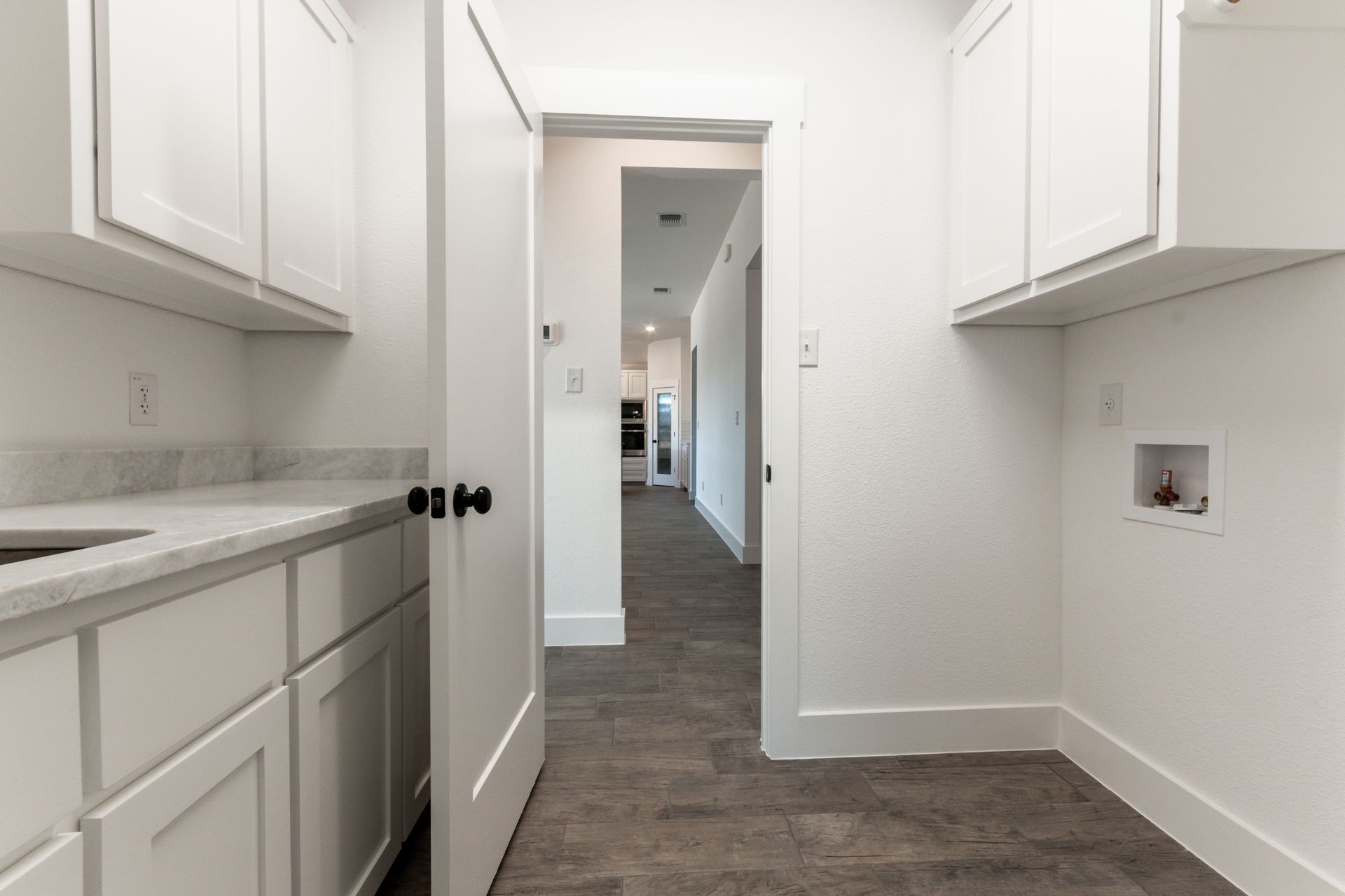 White laundry room with cabinets, counter, and door leading to a hallway.