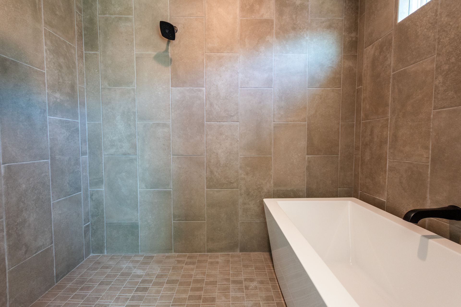 Tiled bathroom with a shower and a rectangular bathtub. Warm tones, bronze showerhead.