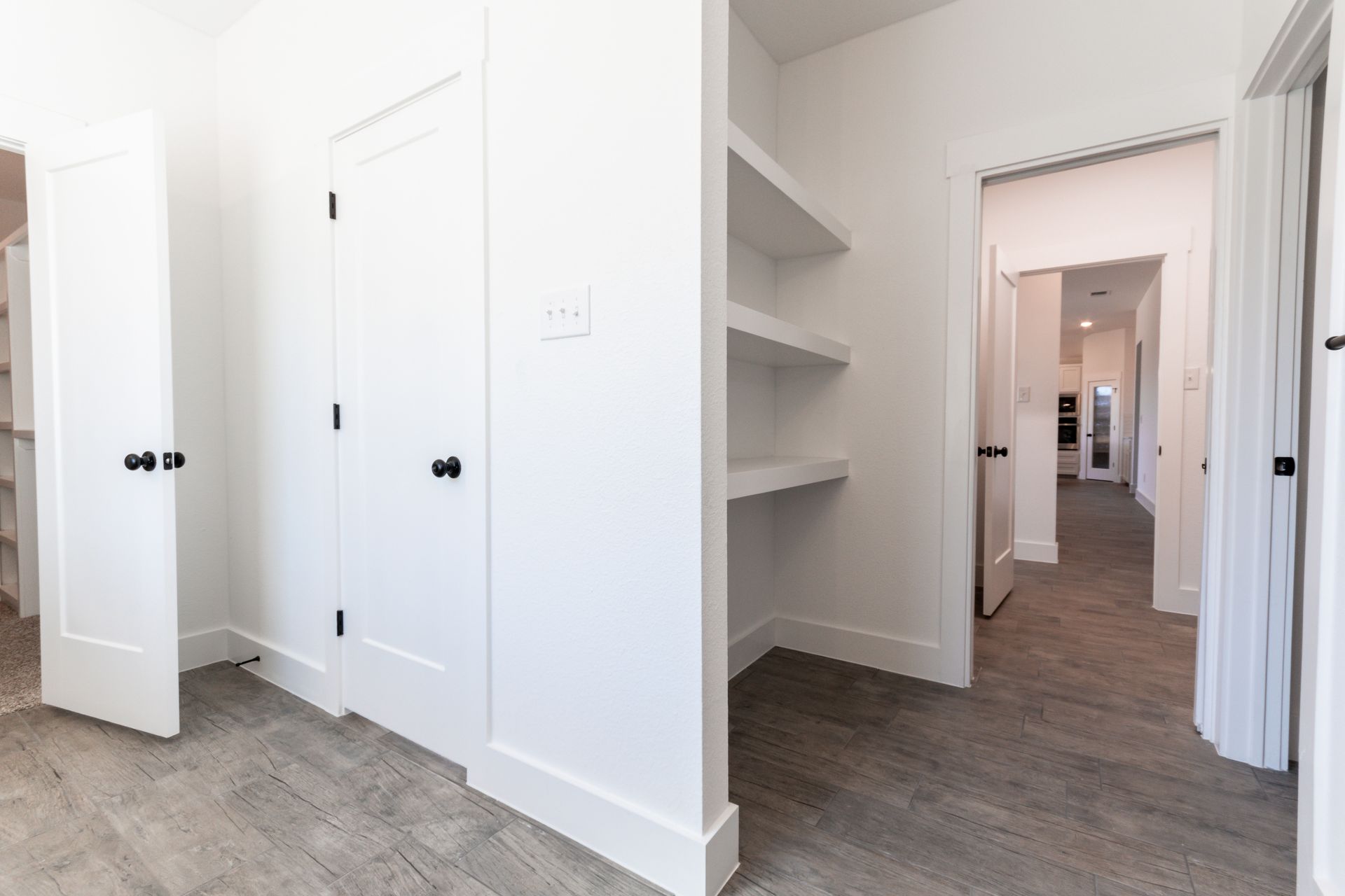 A bright white hallway with multiple doors, built-in shelves, and a view into another room.