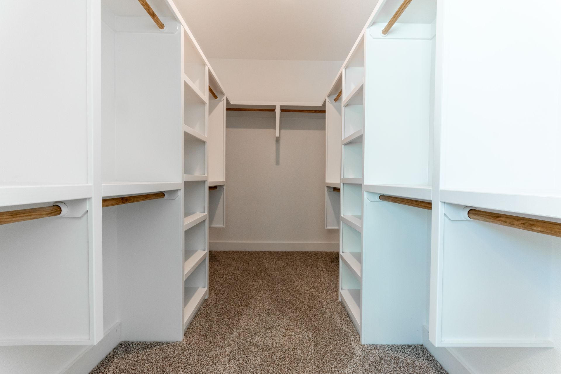 Empty white walk-in closet with shelves and hanging rods; carpeted floor.