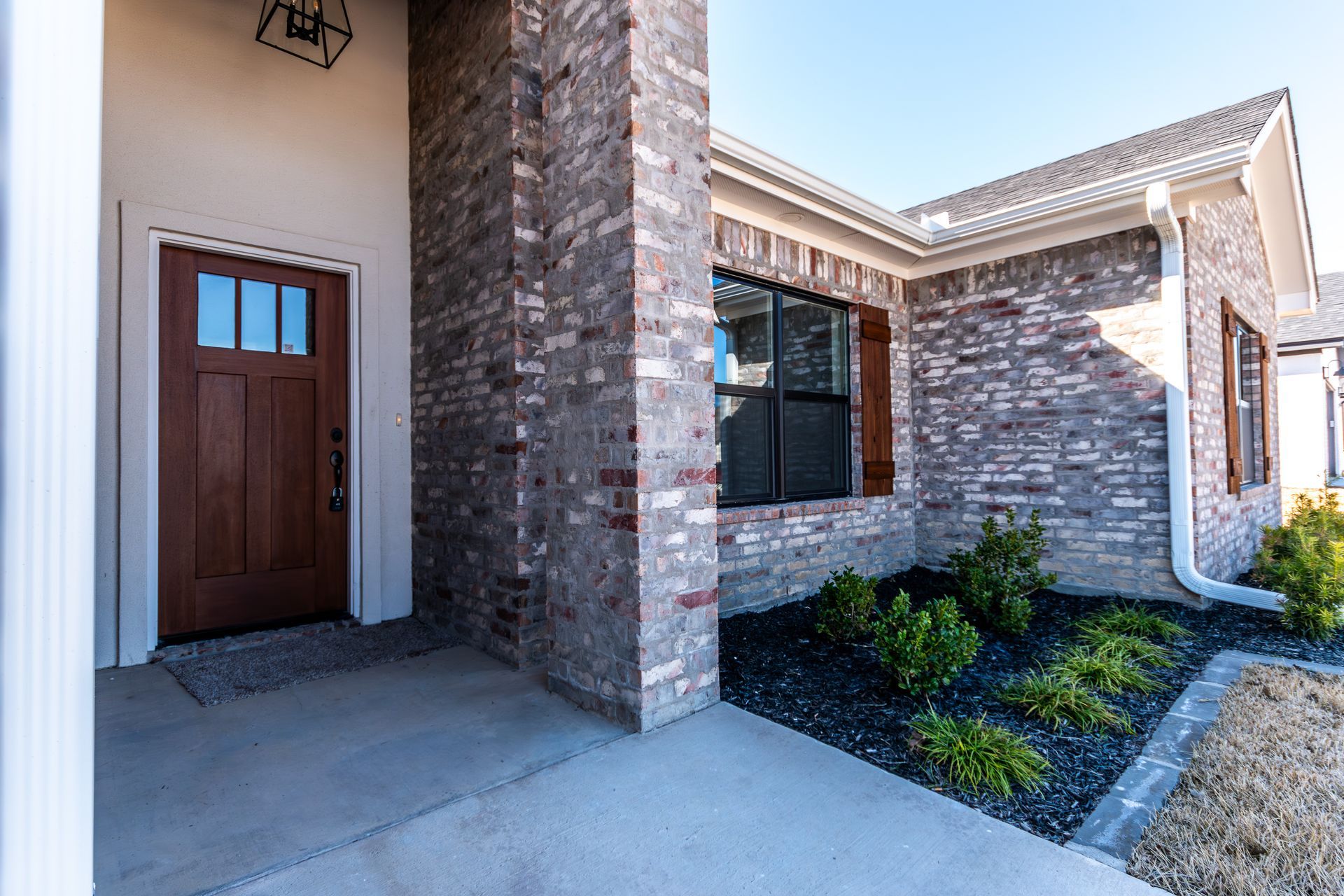 Brick home entrance with brown door, dark-framed window, and black mulch landscaping.