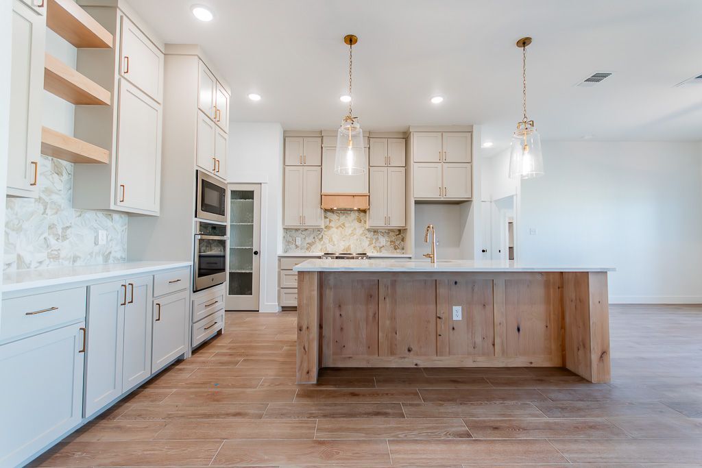 Modern kitchen with light wood island, white cabinets, and pendant lights.