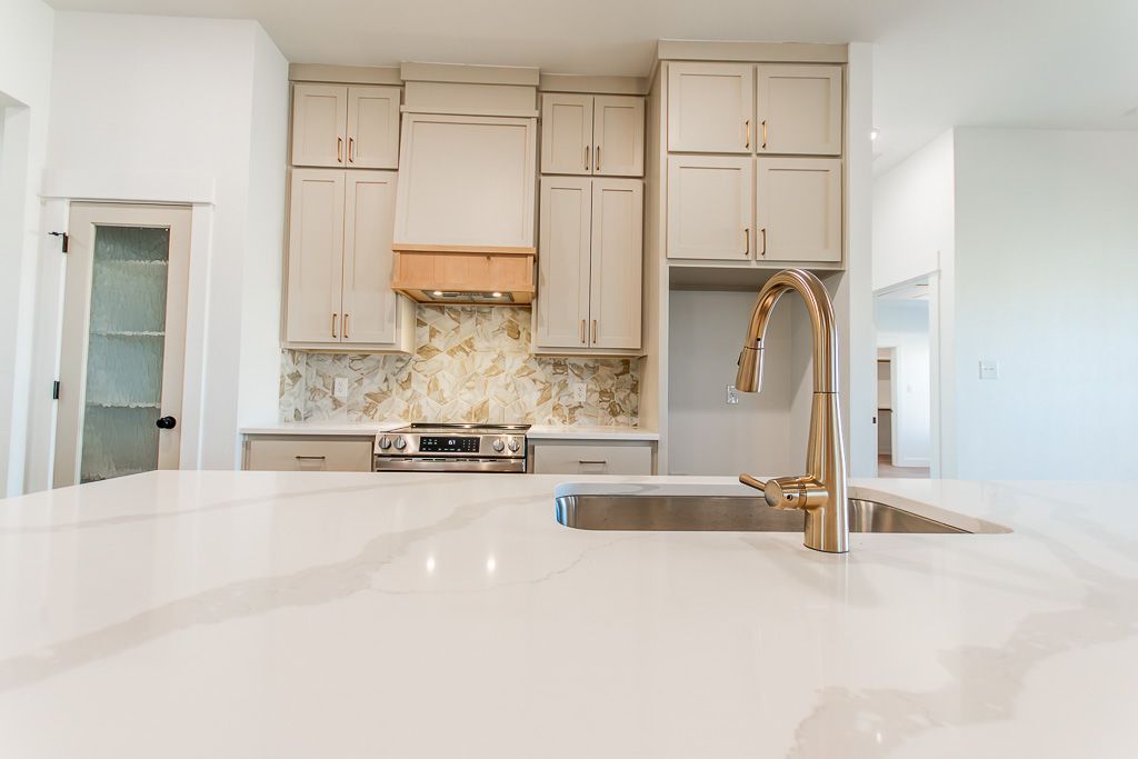 Modern kitchen with white countertops, gold faucet, and light-colored cabinetry.