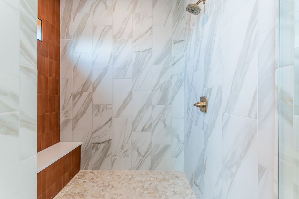 A tiled shower with white marble walls, a bronze shower head and fixtures, and a terracotta wall with a built-in bench.