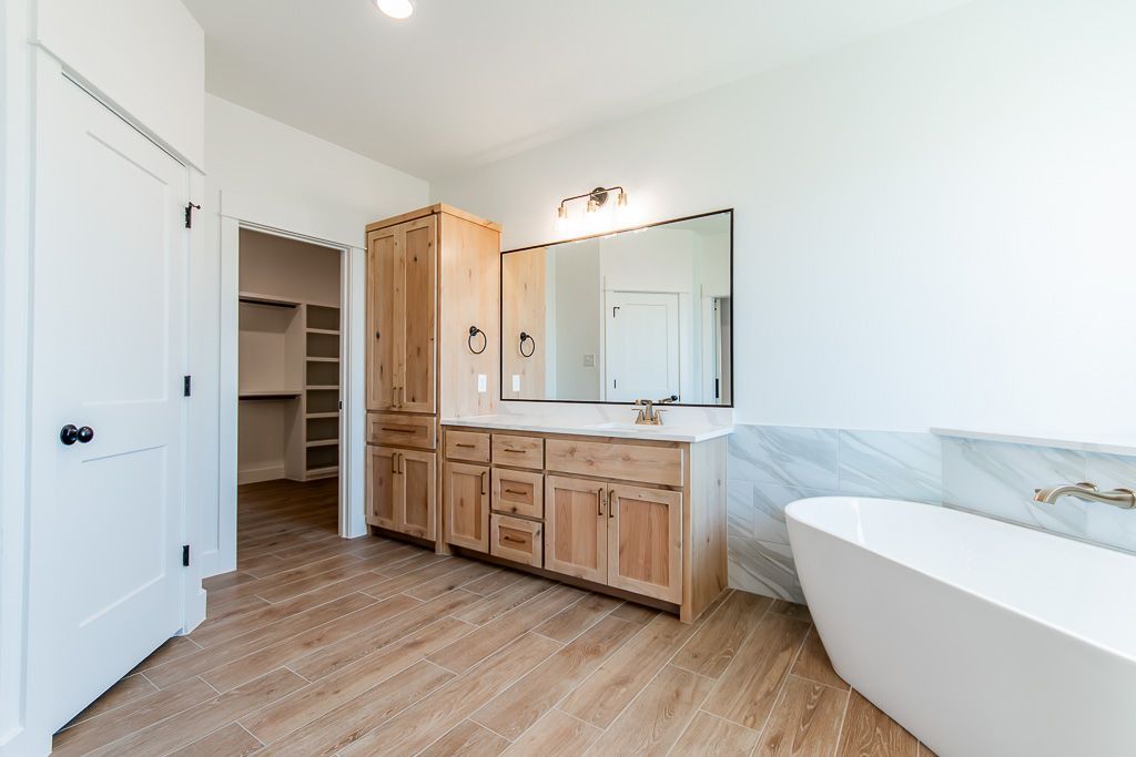 Bathroom with wood cabinets, white bathtub, and light wood-look tile floor.