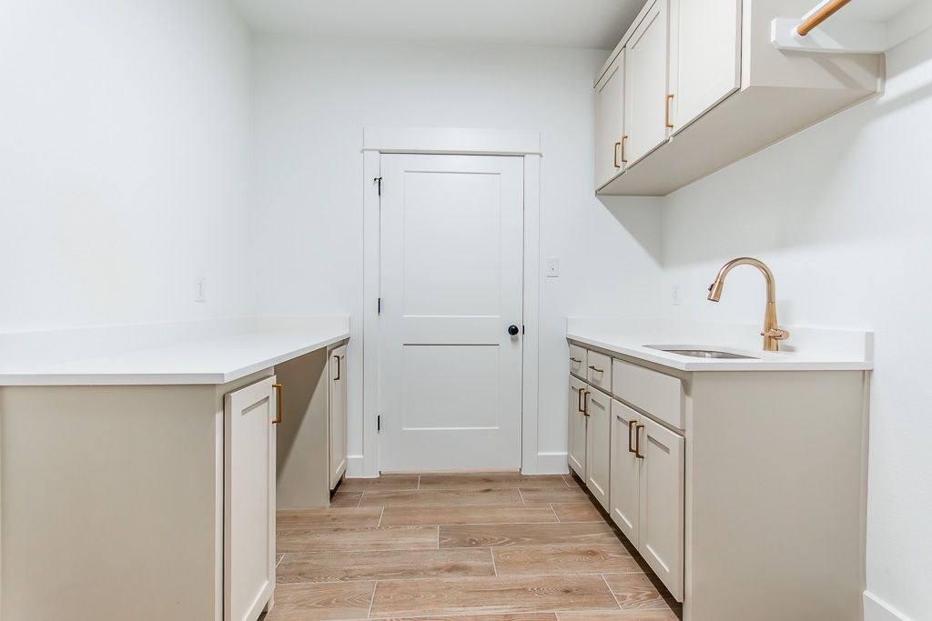 Laundry room with white cabinets, countertop, sink, gold faucet, and door.