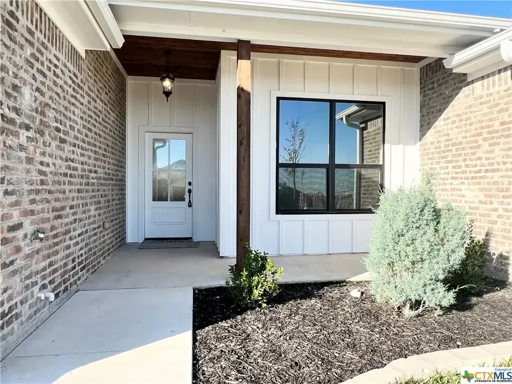 Brick home exterior with white door, window, and decorative wood beam.