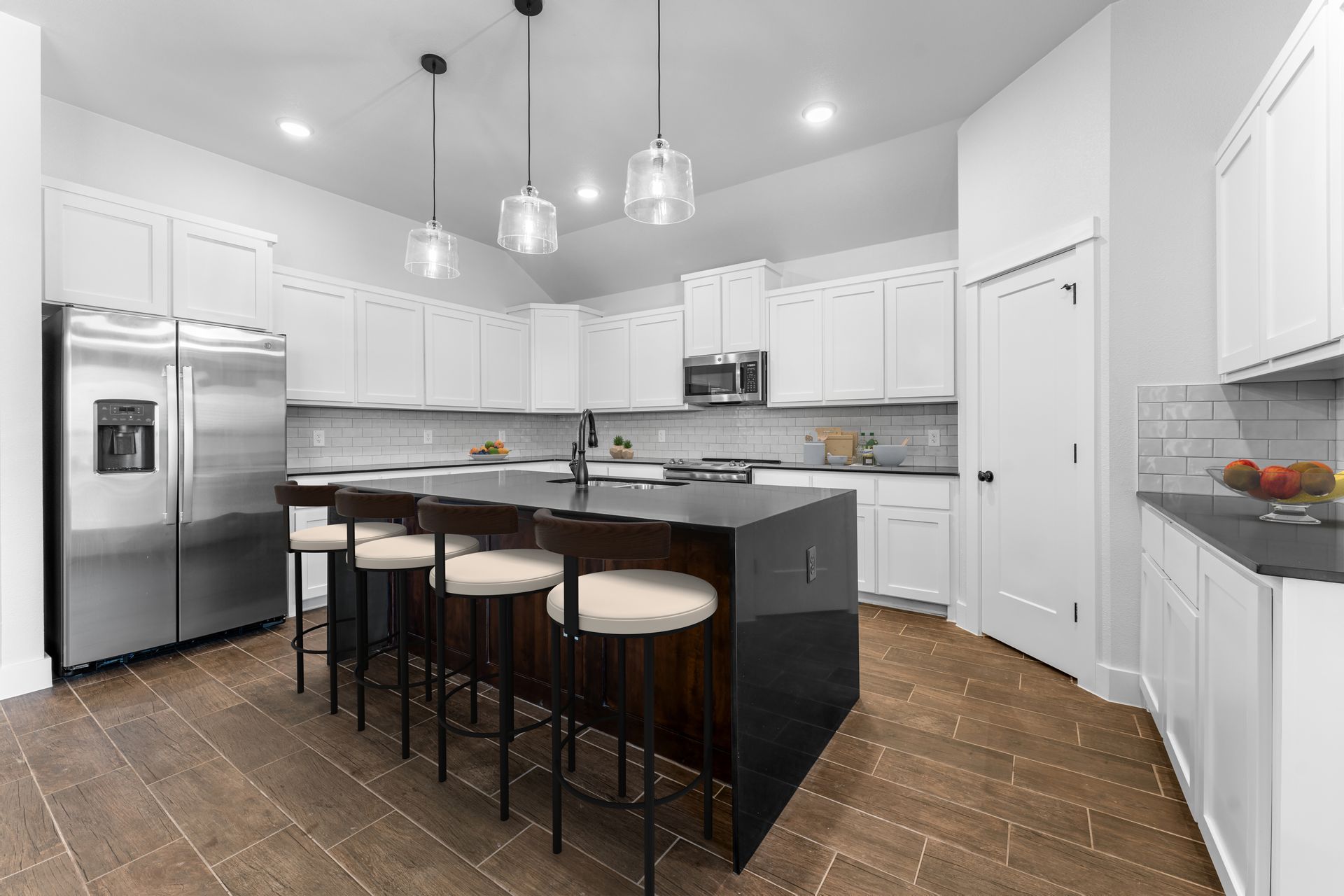 Modern kitchen with white cabinets, dark island with seating, stainless steel appliances, and wood floors.