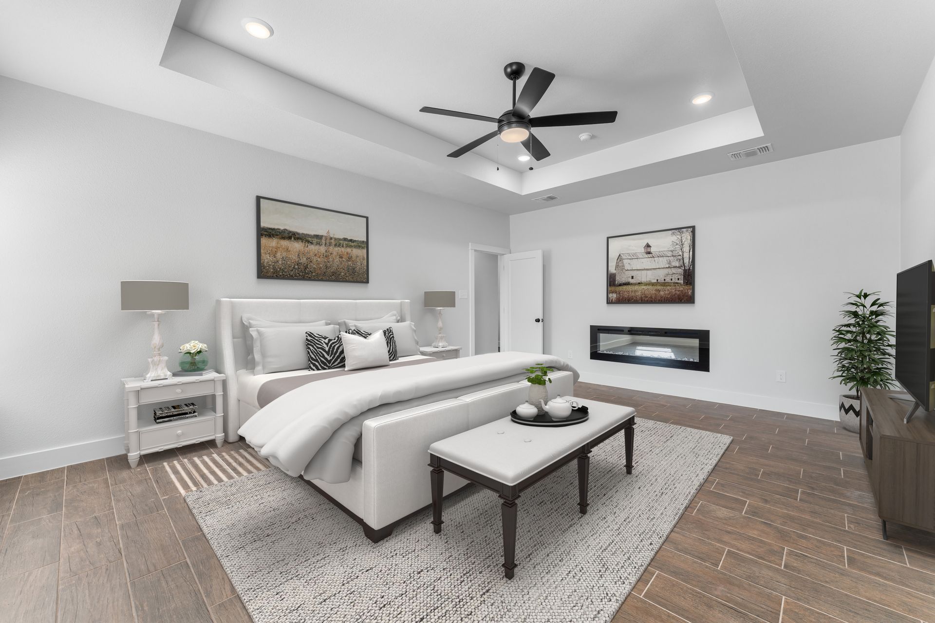 Bedroom with white walls, bed, rug, fireplace, TV, and ceiling fan.