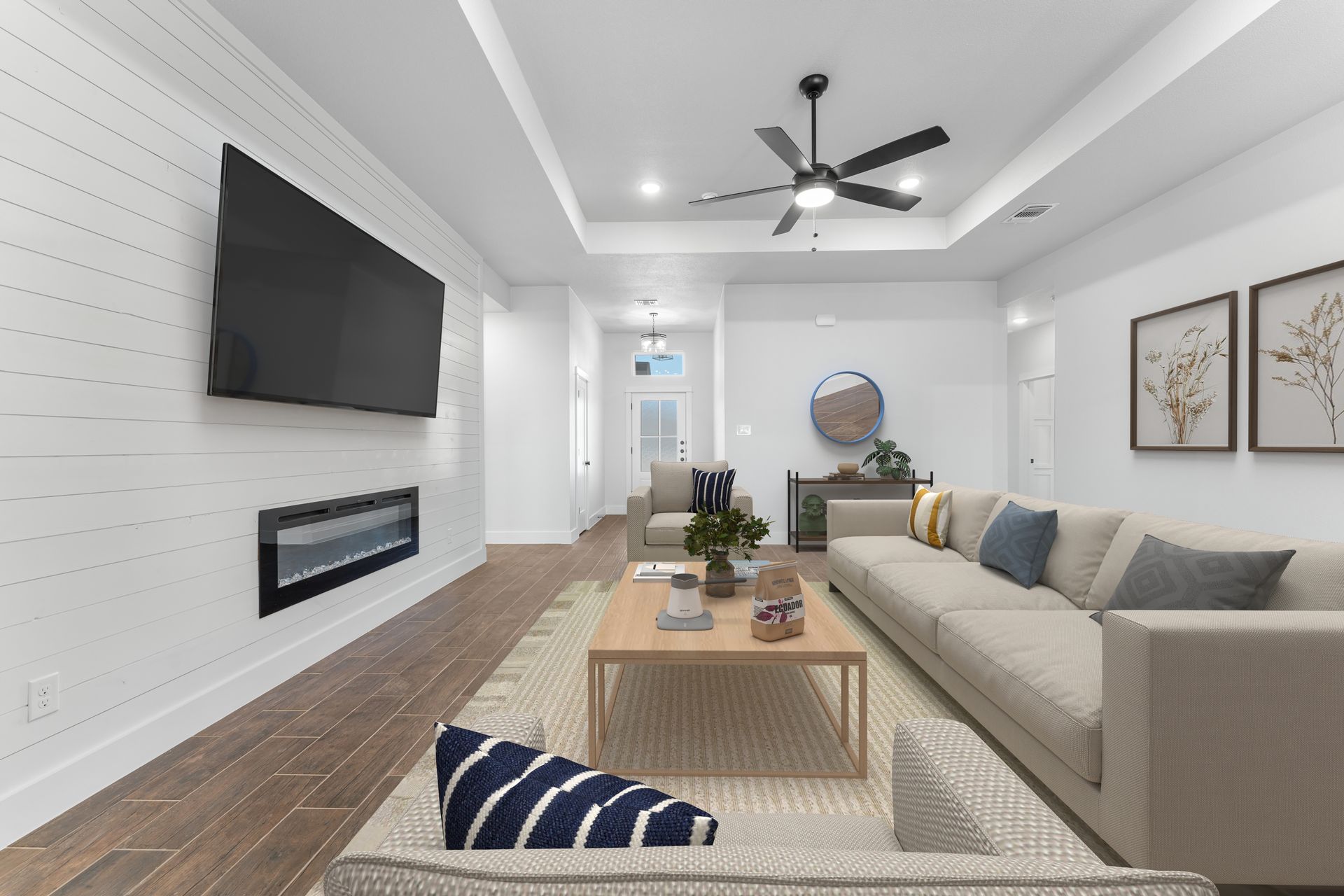 Modern living room with white walls, fireplace, and large screen TV. Beige sofa, wooden floor.