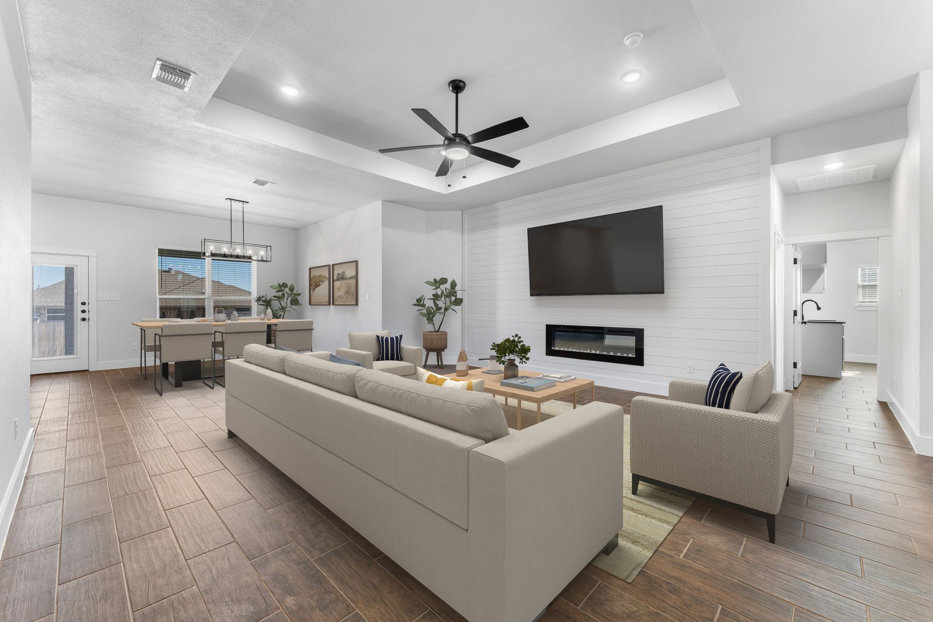 Living room with beige furniture, TV, fireplace, and dining table; wood floors and white walls.