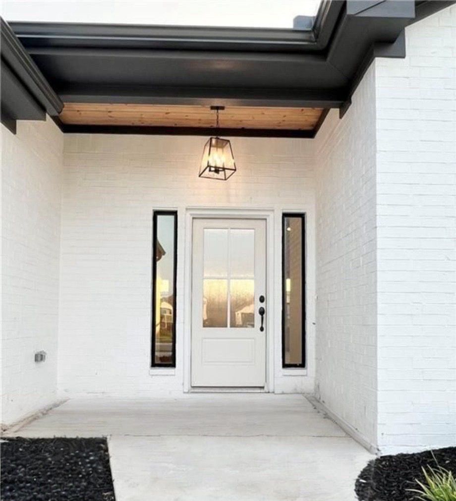 White brick entryway with black trim, a white door, and a hanging light fixture.