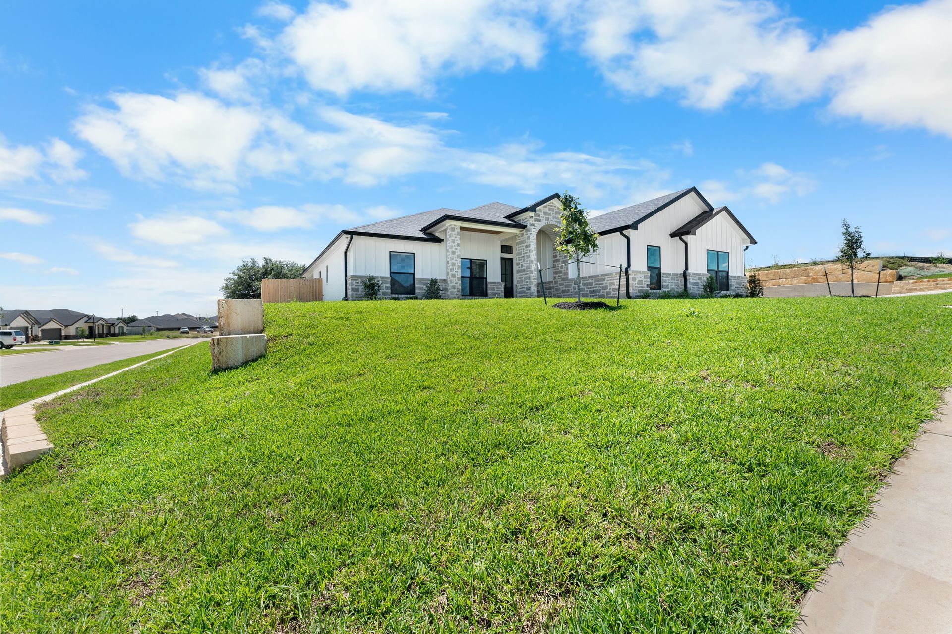 White house with dark roof on a grassy hill under a blue sky with clouds.