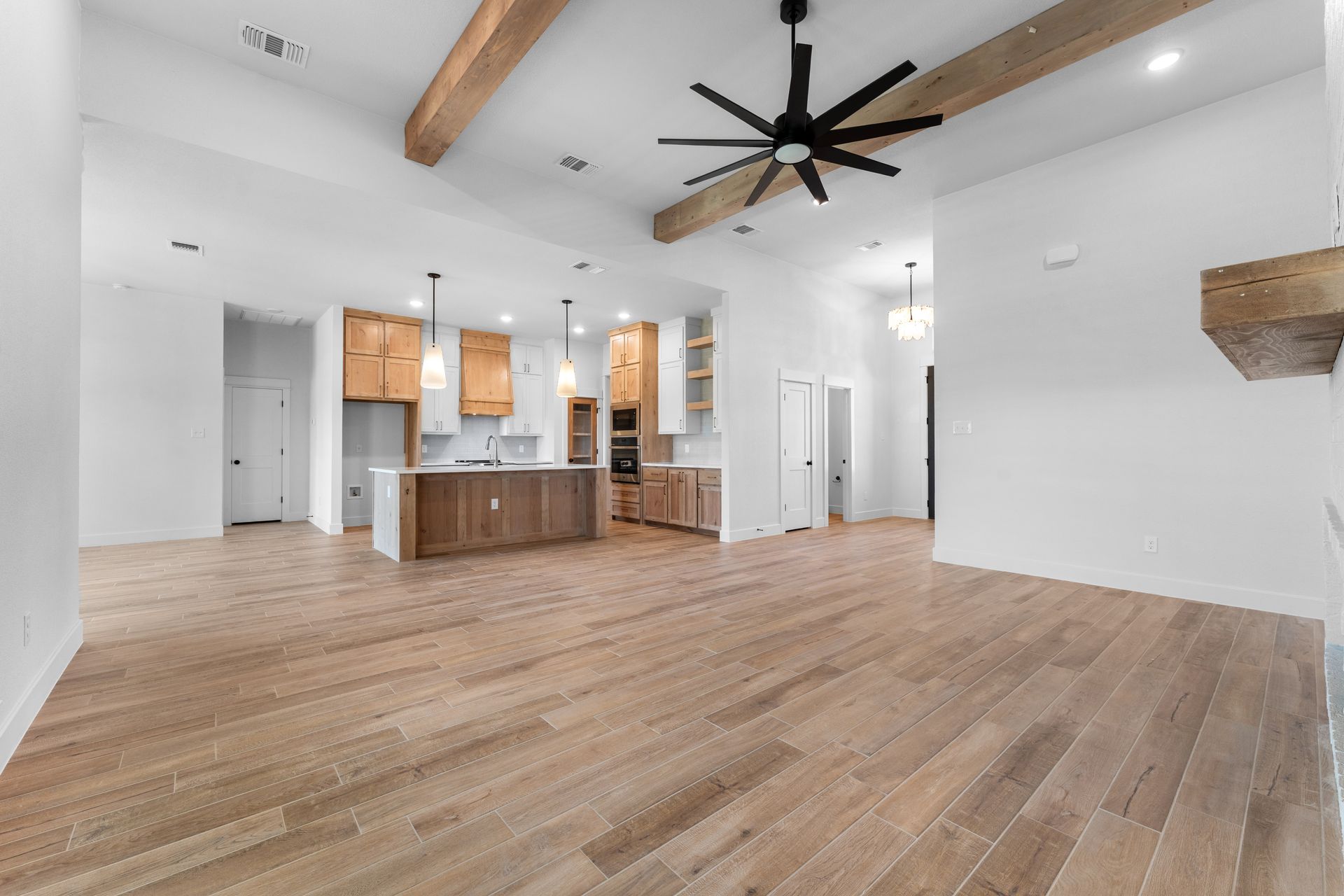 Spacious, light-filled living area with wood floors, kitchen, and exposed wooden beams.
