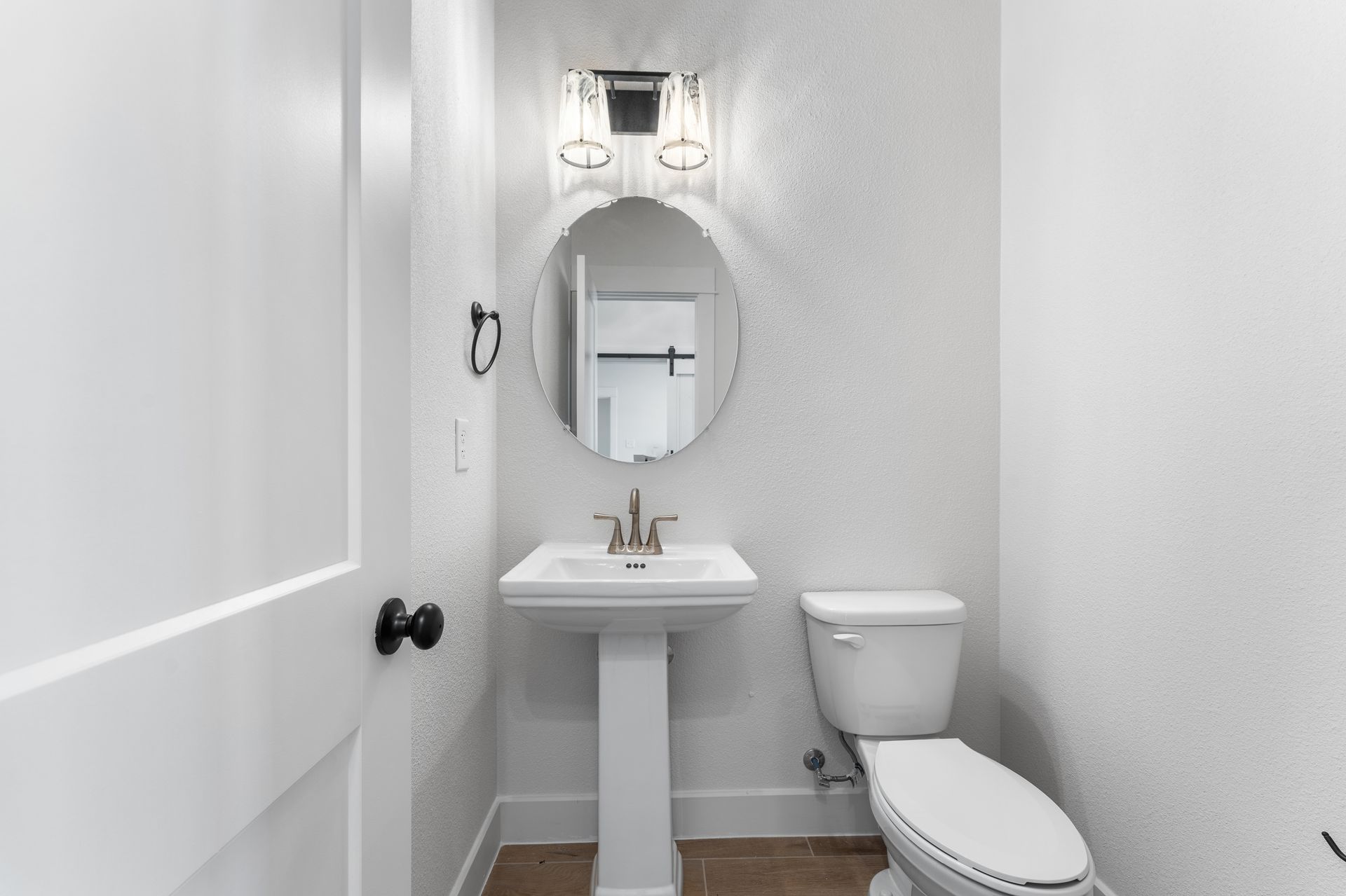 White pedestal sink and toilet in a small, white-walled bathroom with an oval mirror.