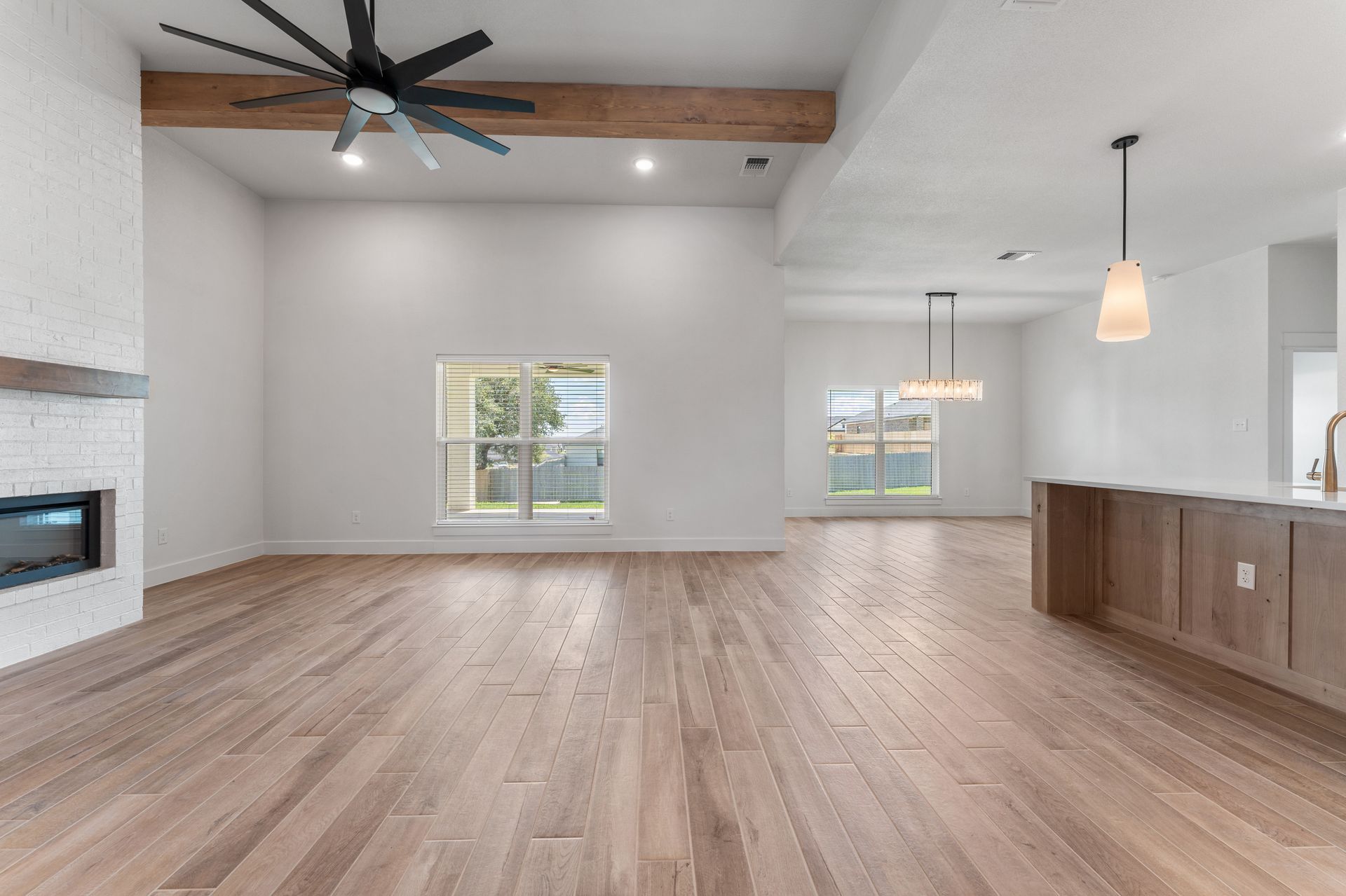 Empty living room with wood floors, fireplace, and high ceilings with wood beam and ceiling fan.