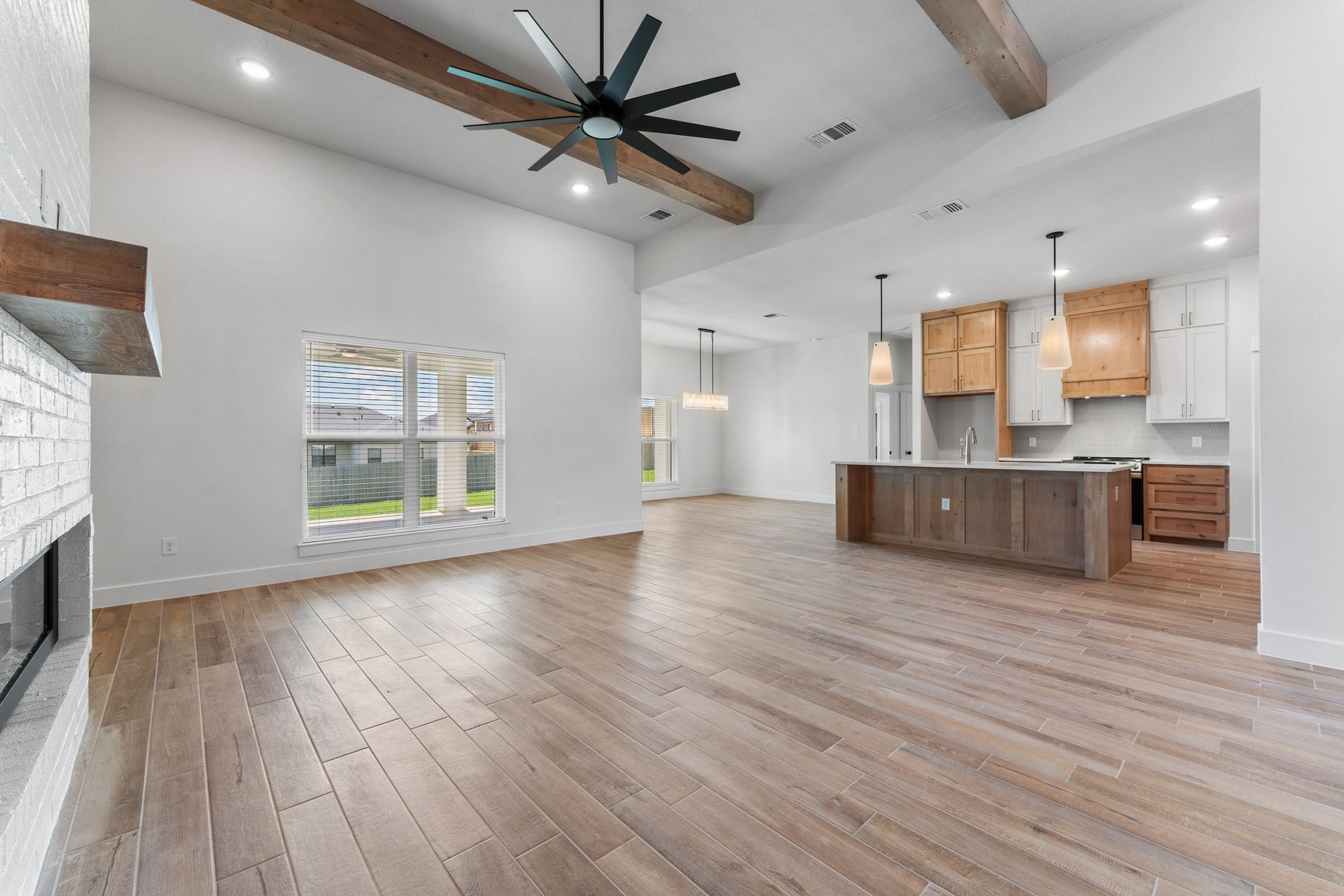 Spacious, light-filled living area with hardwood floors, kitchen, and exposed beams; neutral tones and natural light.