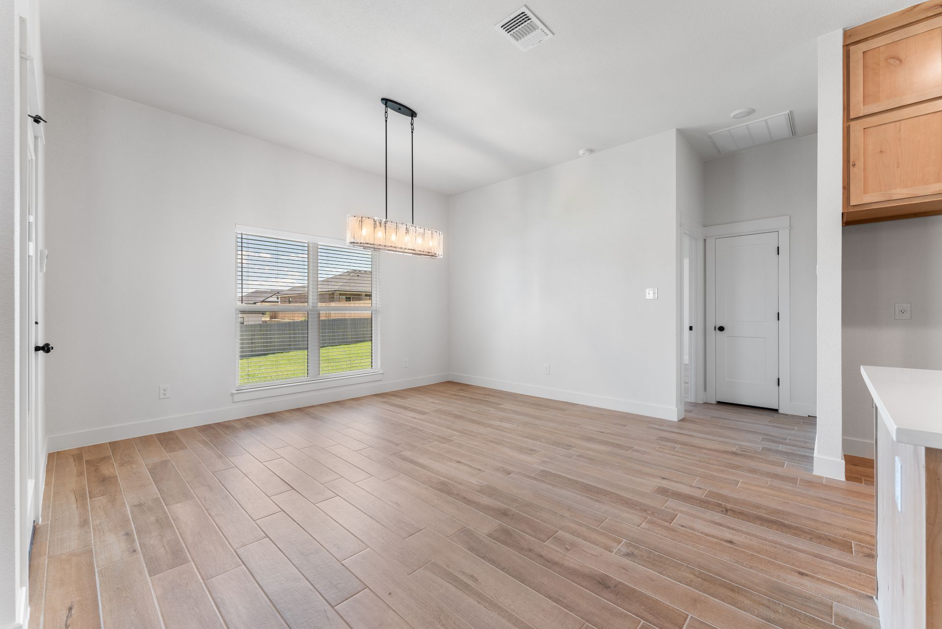 Empty dining room with wood flooring, white walls, and a window.