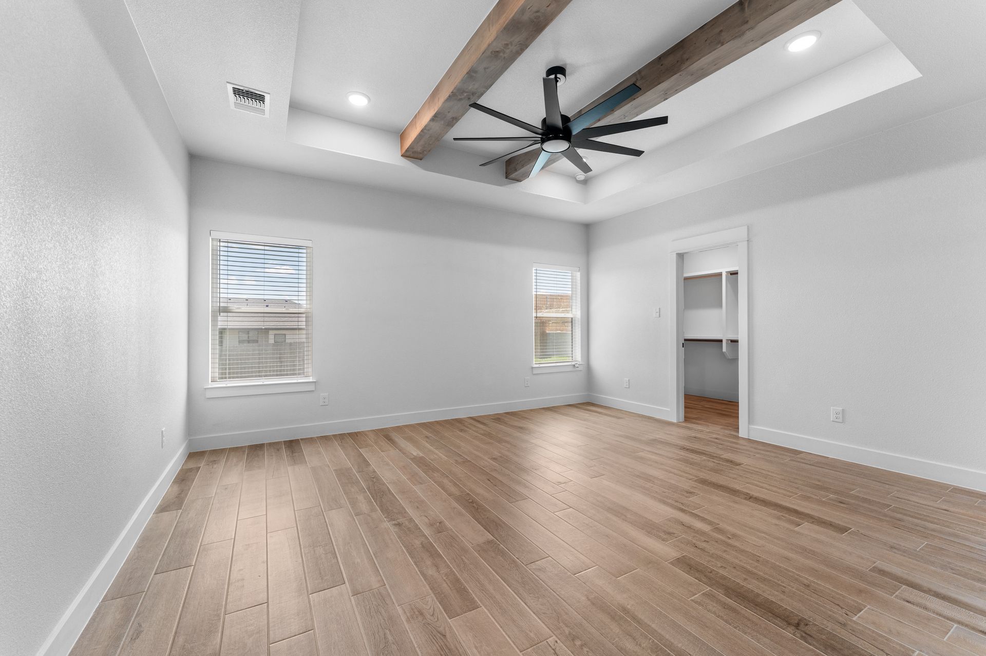 Empty bedroom with hardwood floors, white walls, two windows, and a ceiling fan.