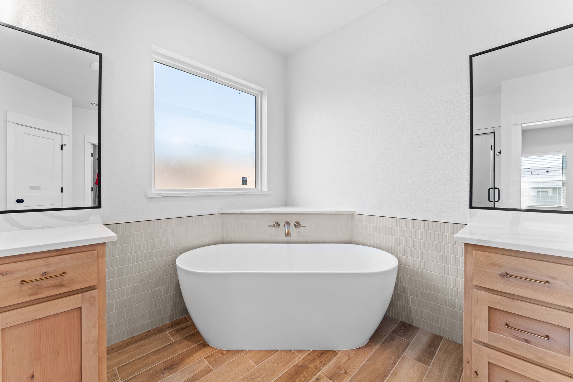 Bathroom with a freestanding tub, wood floor, and two vanities with mirrors.
