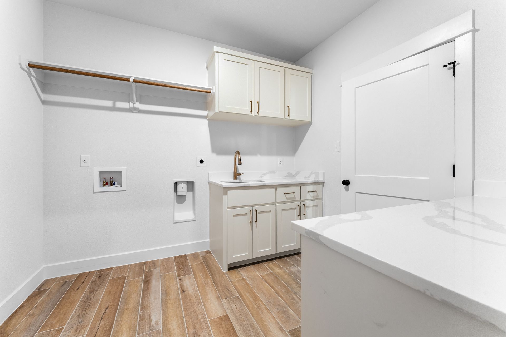 Laundry room with white cabinets, countertop, and door. Wooden floors and clothes rod.