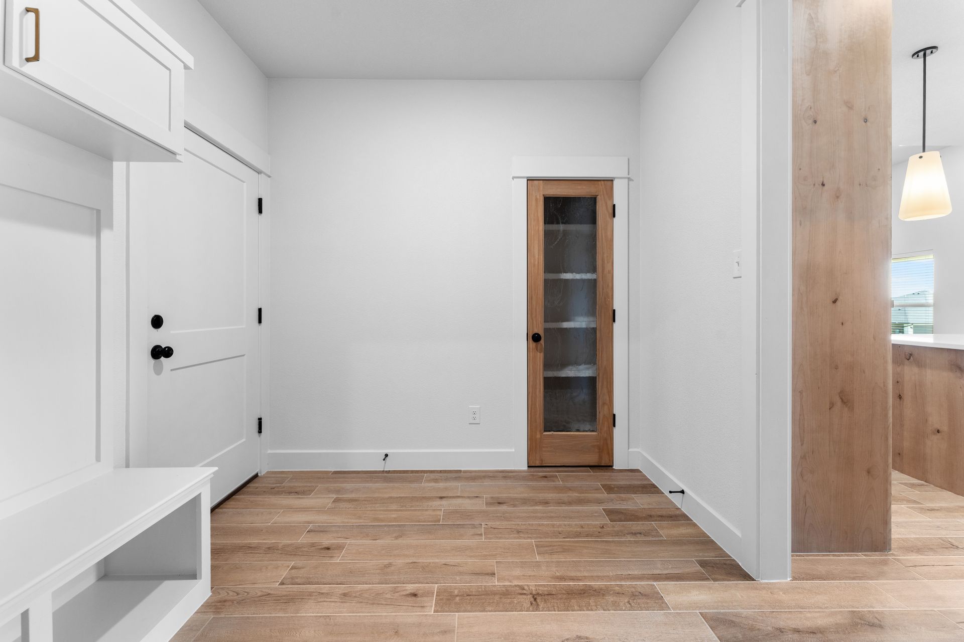 Entryway with white walls, light wood flooring, a storage bench, and a glass-paneled door.