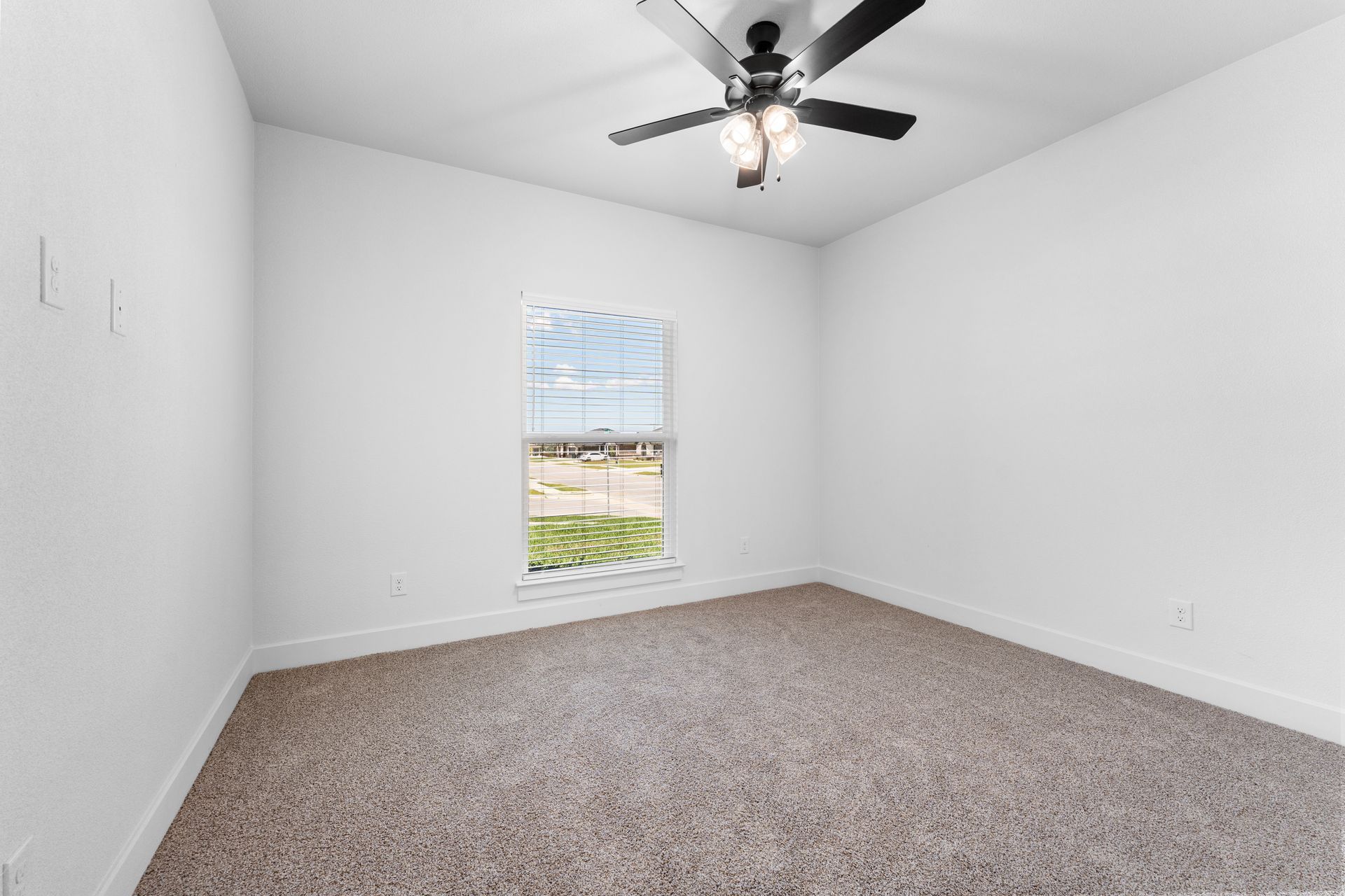 Empty bedroom with light brown carpet, white walls, and a window with a view. A ceiling fan is installed.