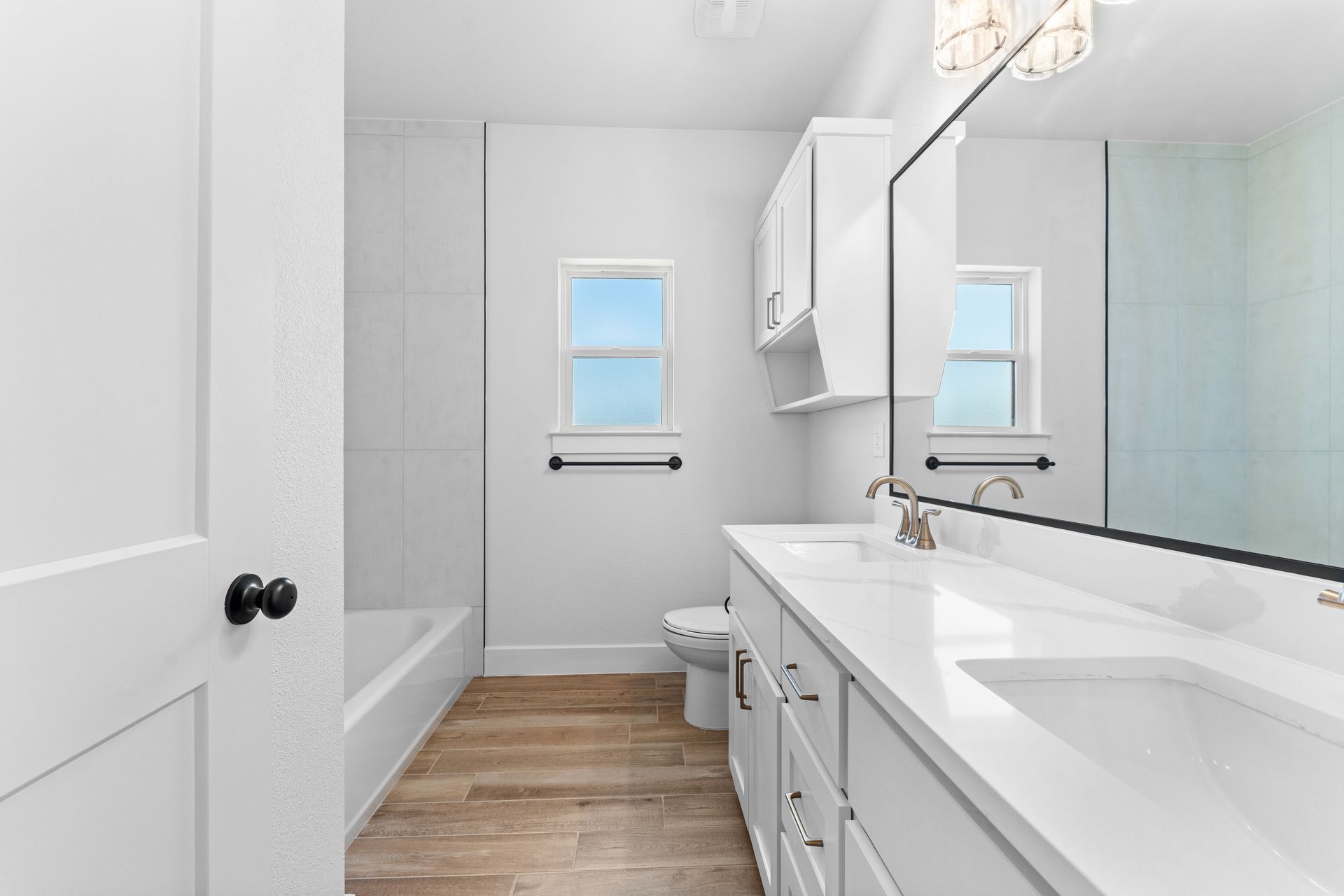 White bathroom with double vanity, bathtub, and small window.