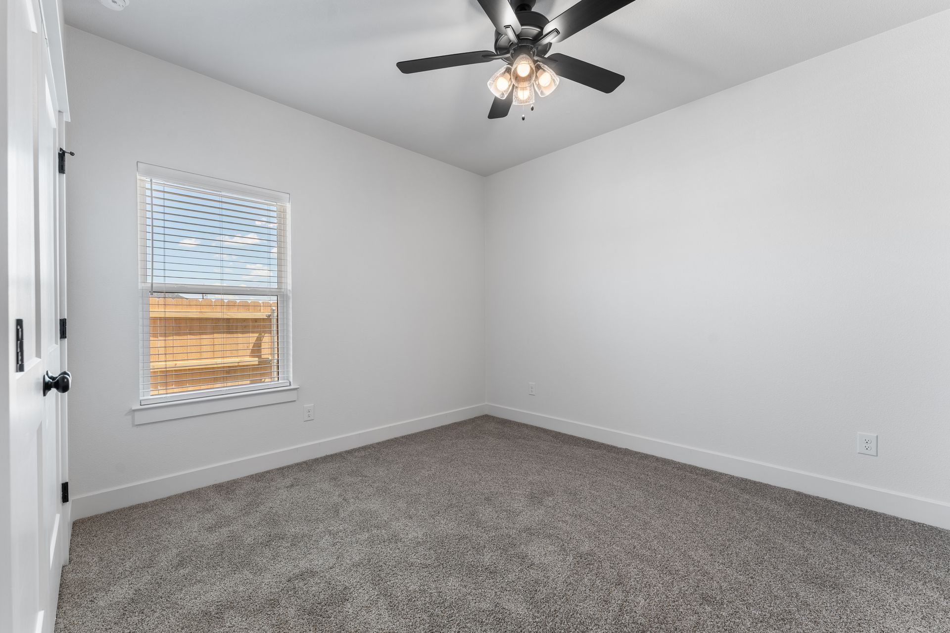 Empty bedroom with light gray carpet, white walls, window, and ceiling fan.
