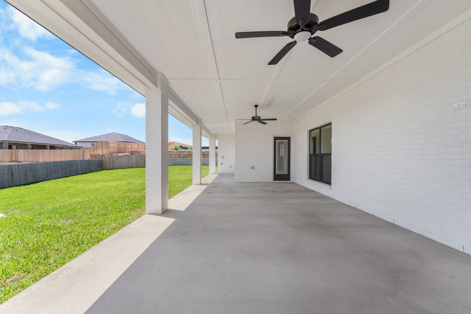 Covered patio with a concrete floor, white pillars, and ceiling fans overlooking a grassy backyard.
