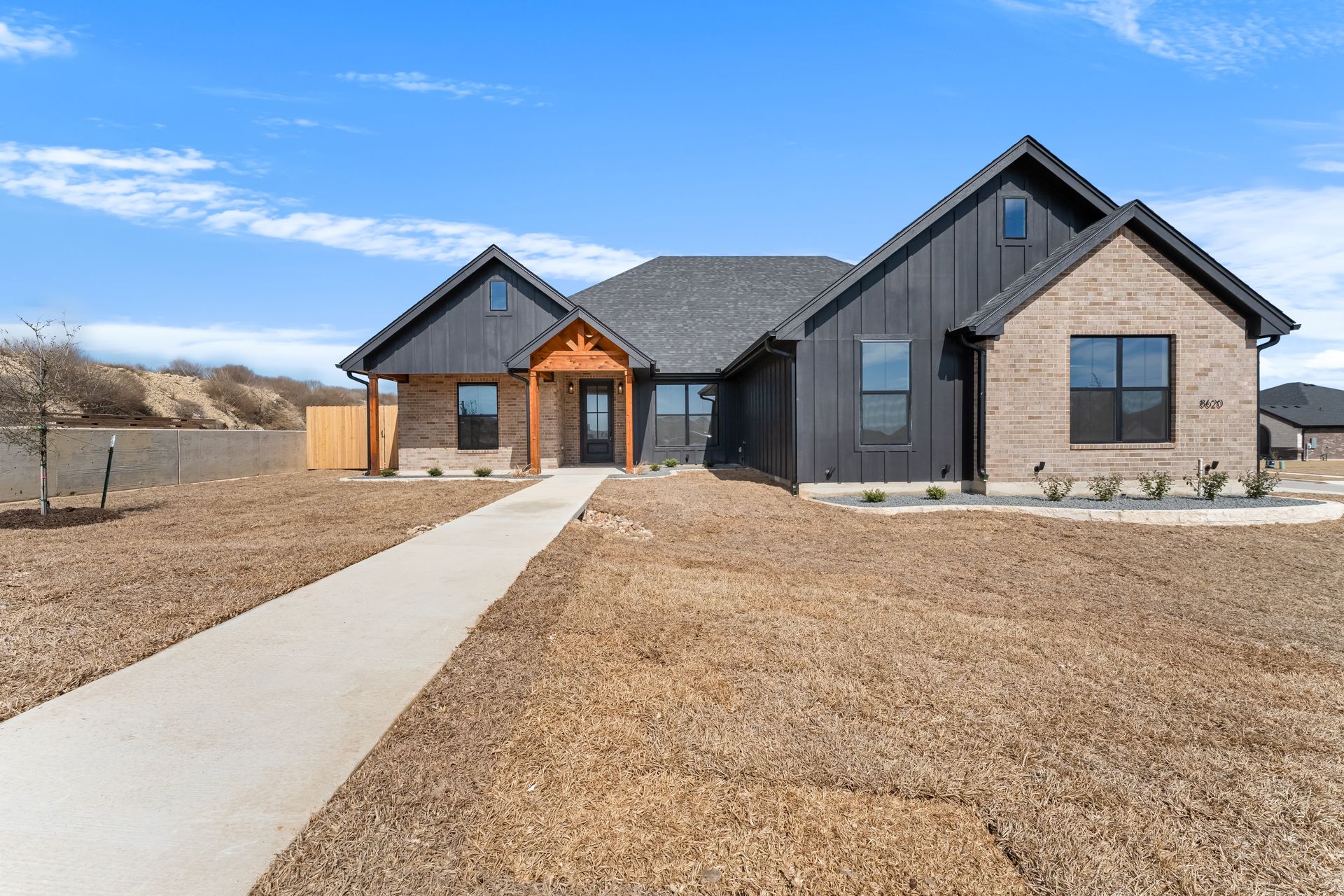 Brick and white house with attached garage and dry brown grass yard.