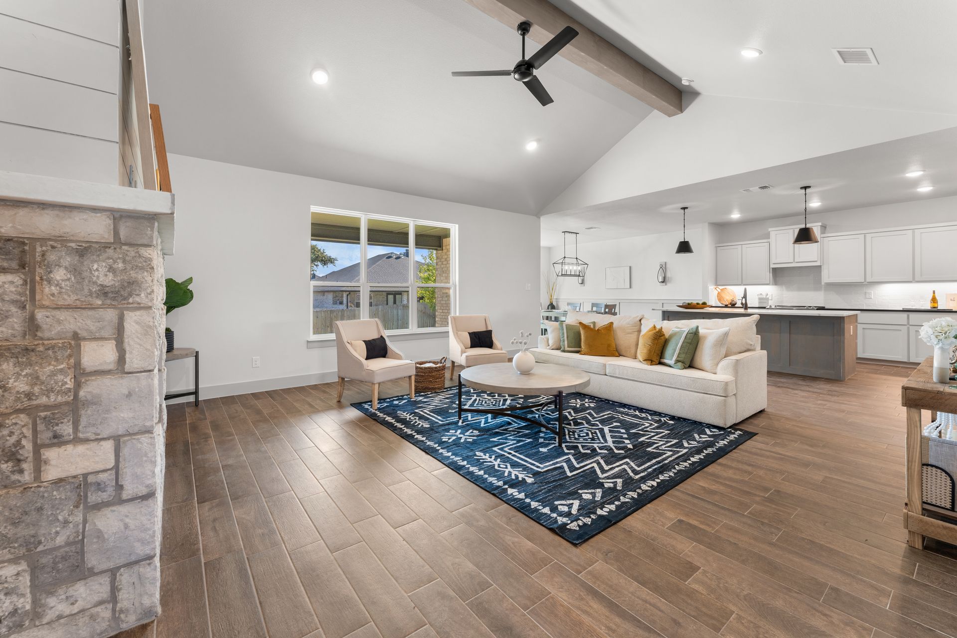 Living room with vaulted ceiling, hardwood floors, and a blue patterned rug.