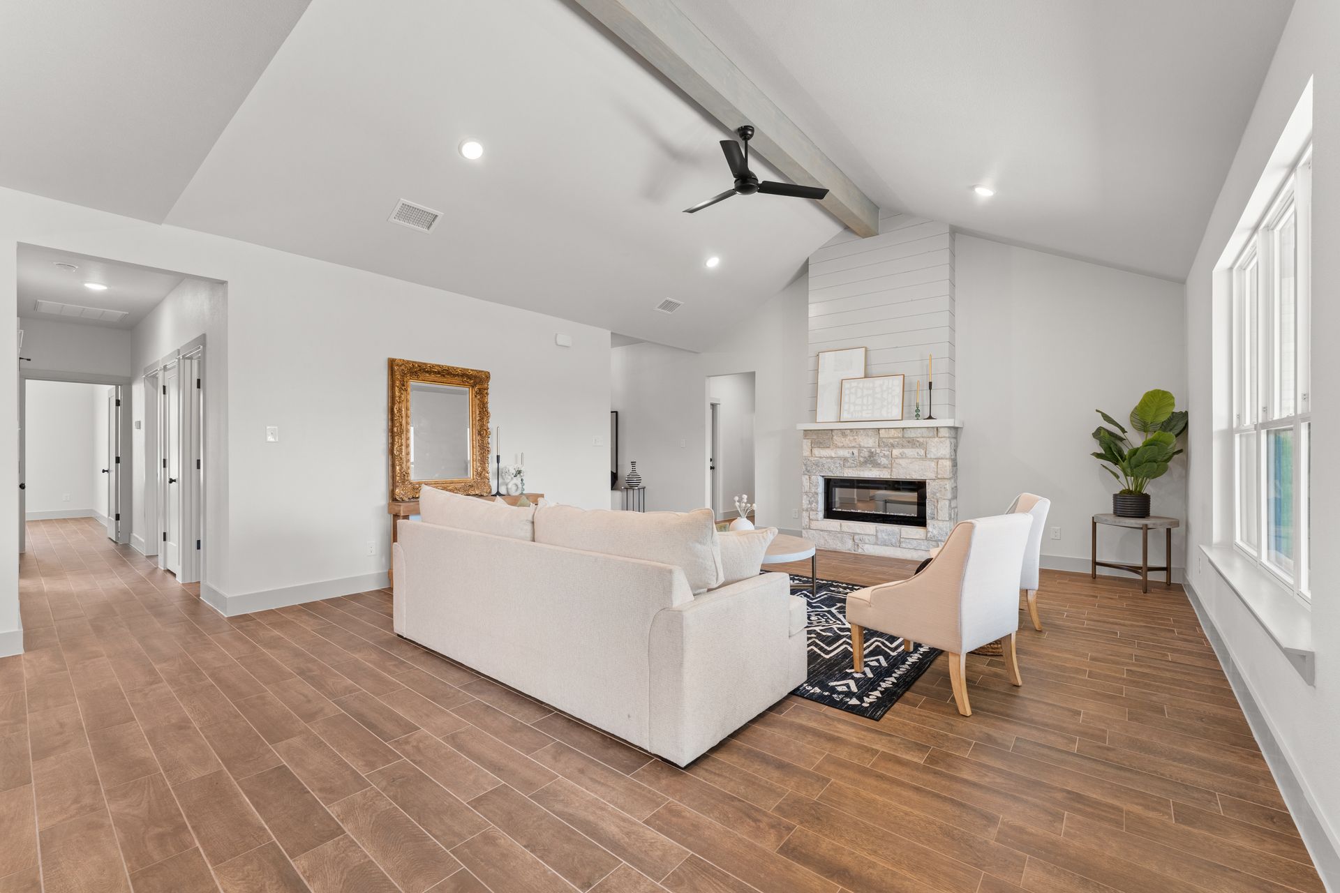 Spacious living room with white walls, fireplace, sofa, chairs, wooden floor, and a large mirror.