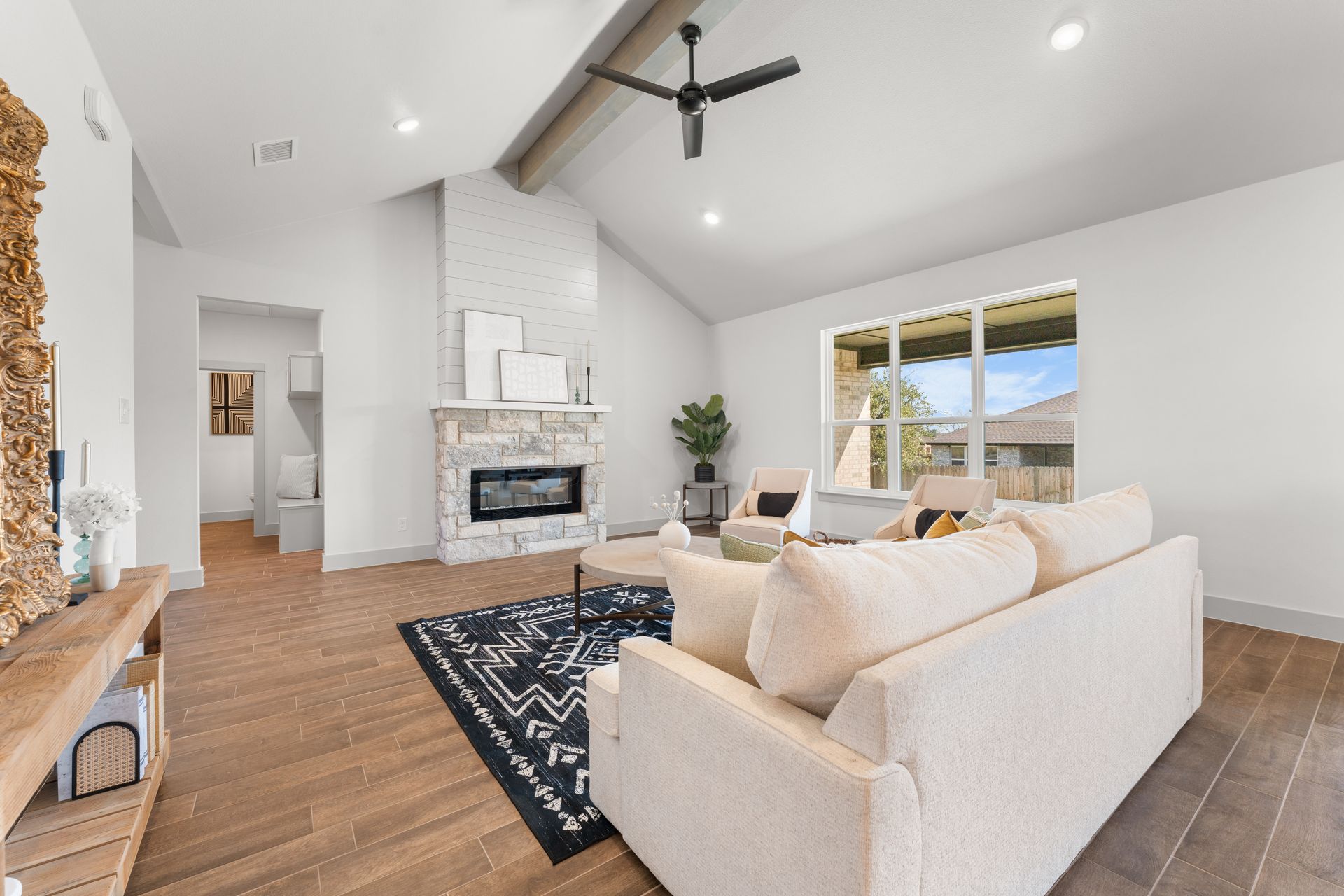 Living room with vaulted ceiling, fireplace, and sofa, natural wood floors, and large window.
