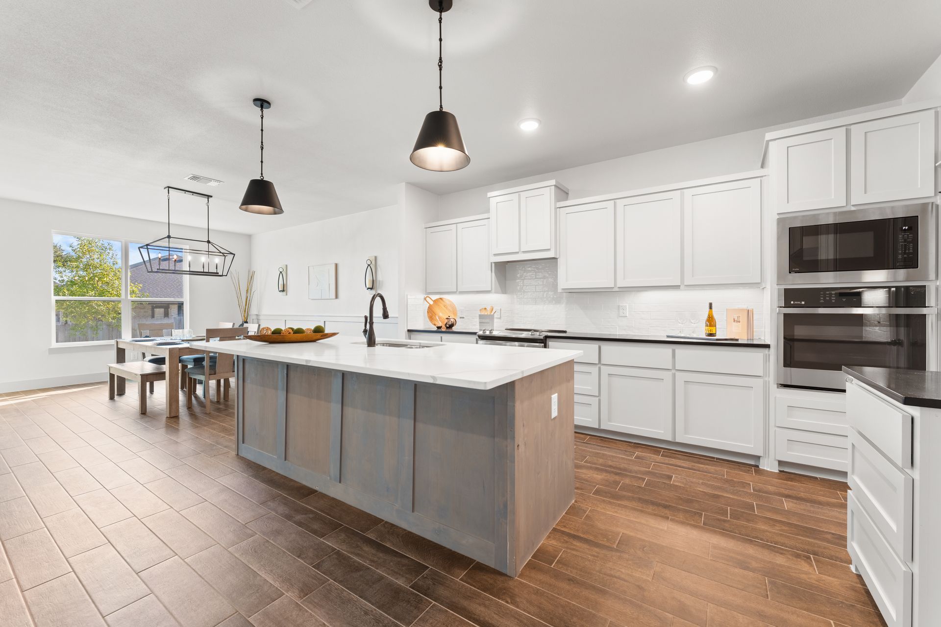 Modern kitchen with white cabinets, gray island, stainless steel appliances, and wood floors.