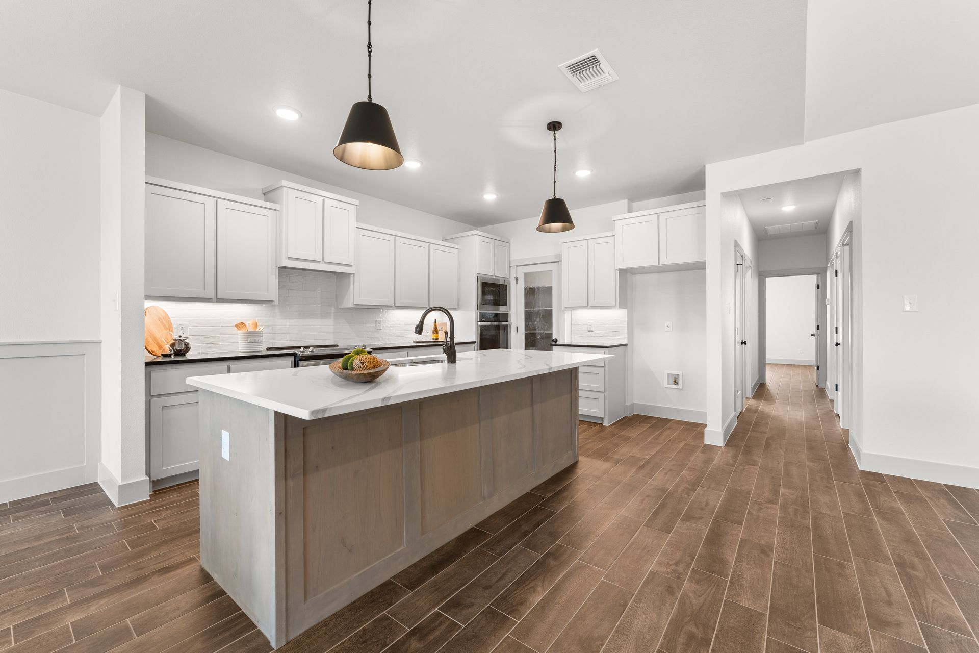 Modern kitchen with island, gray cabinets, black pendant lights, and wood floors.