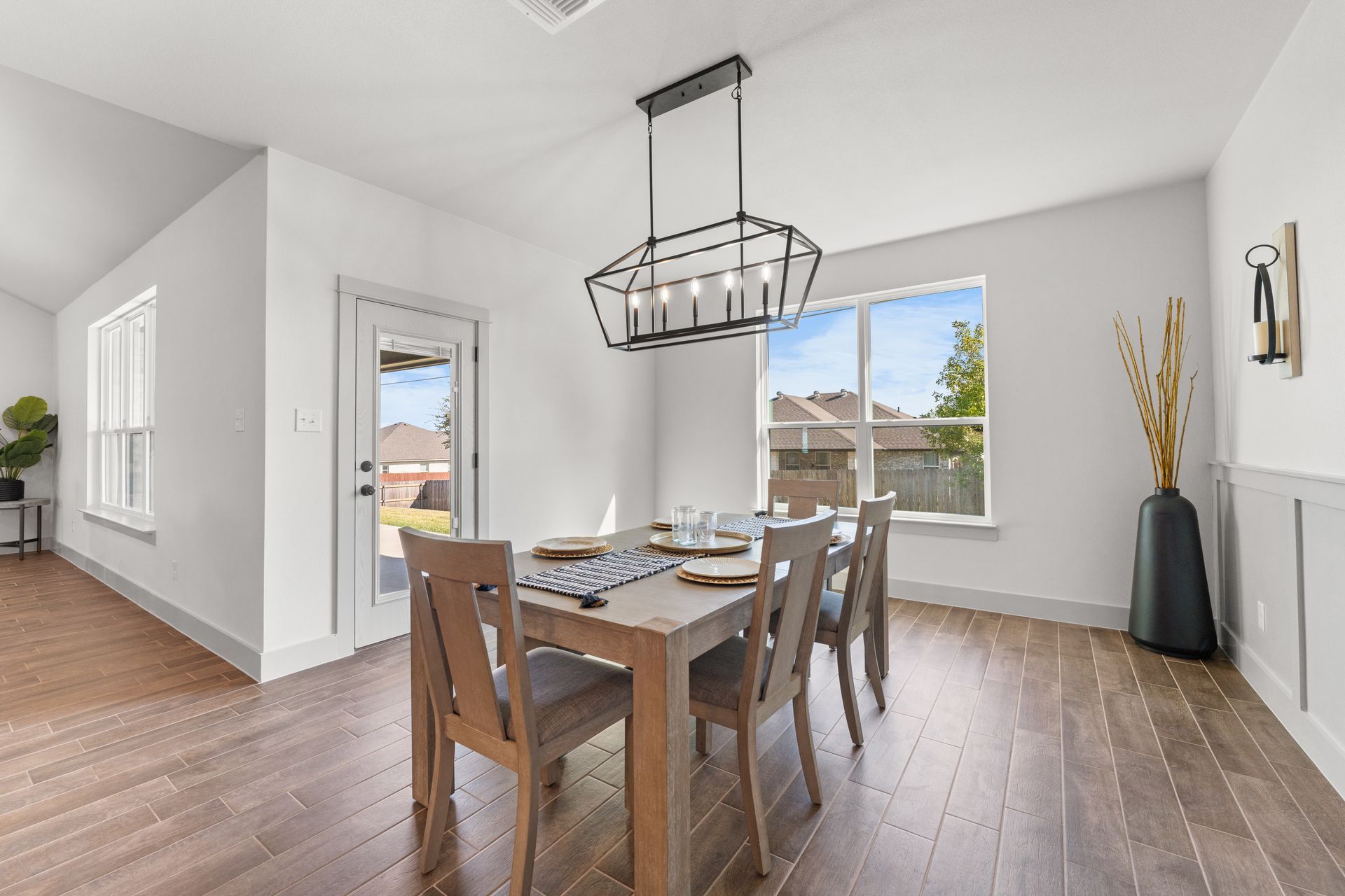 Dining room with wooden table, chairs, and pendant light. Large windows and door.