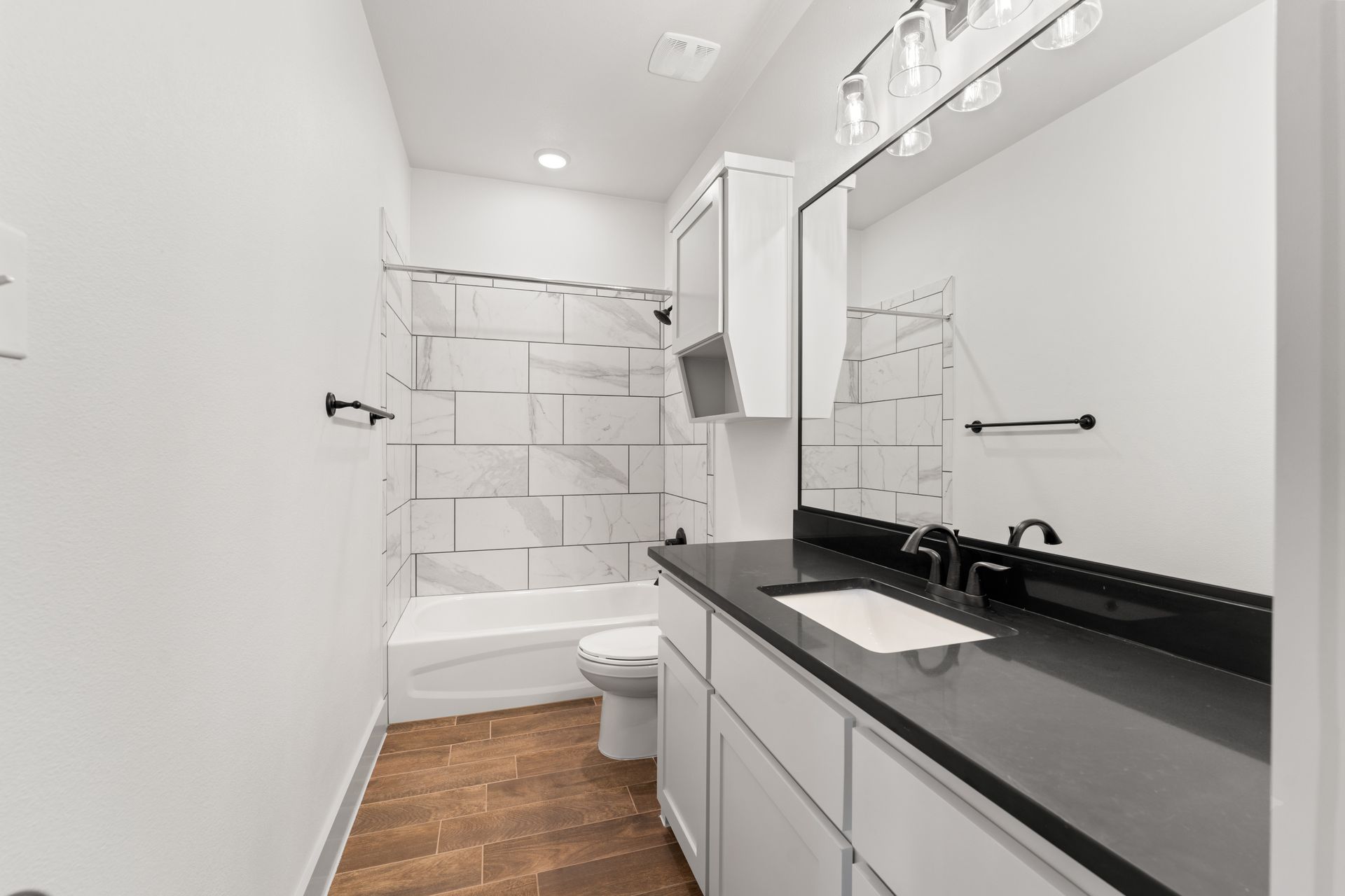 Bathroom with white walls, black countertop, white vanity, marble tile shower, and wood-look floor.