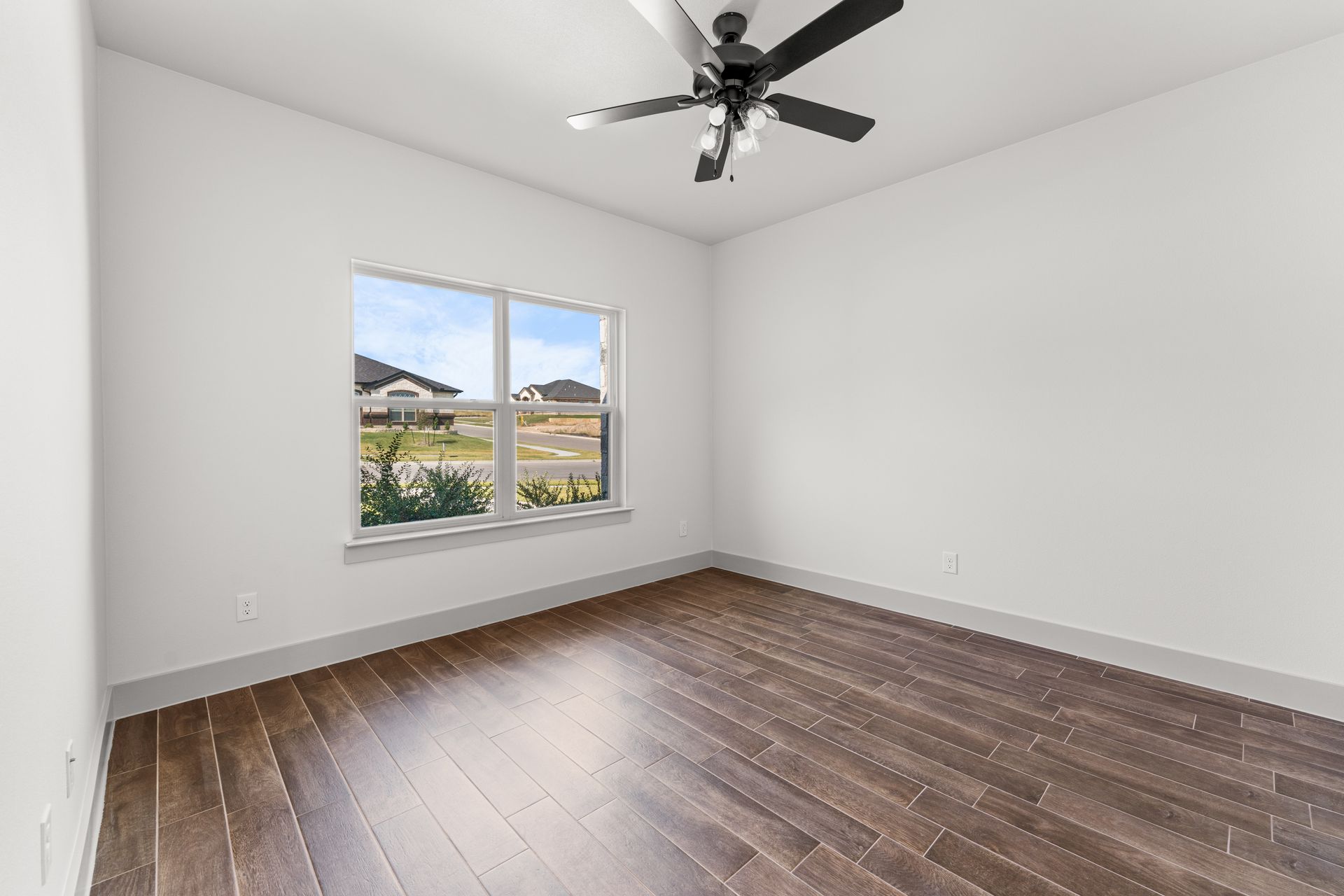 Empty room with dark wood floor, white walls, window, and ceiling fan.
