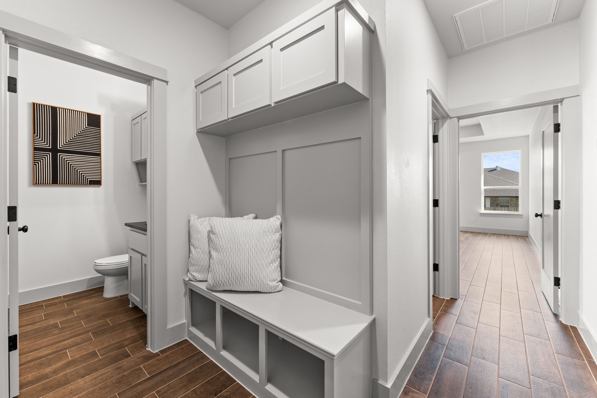 Hallway with built-in bench, overhead storage, and doors leading to rooms. White and wood tones.