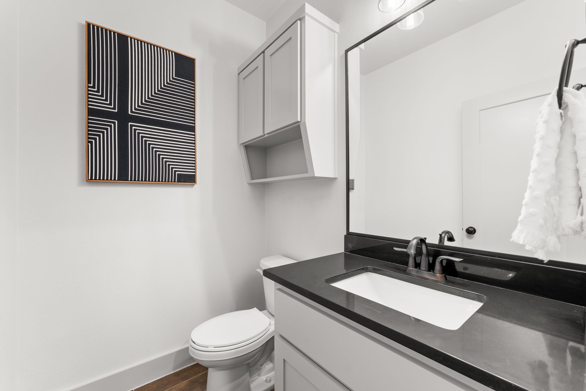 Modern bathroom with white walls, black countertop, art, and cabinet.
