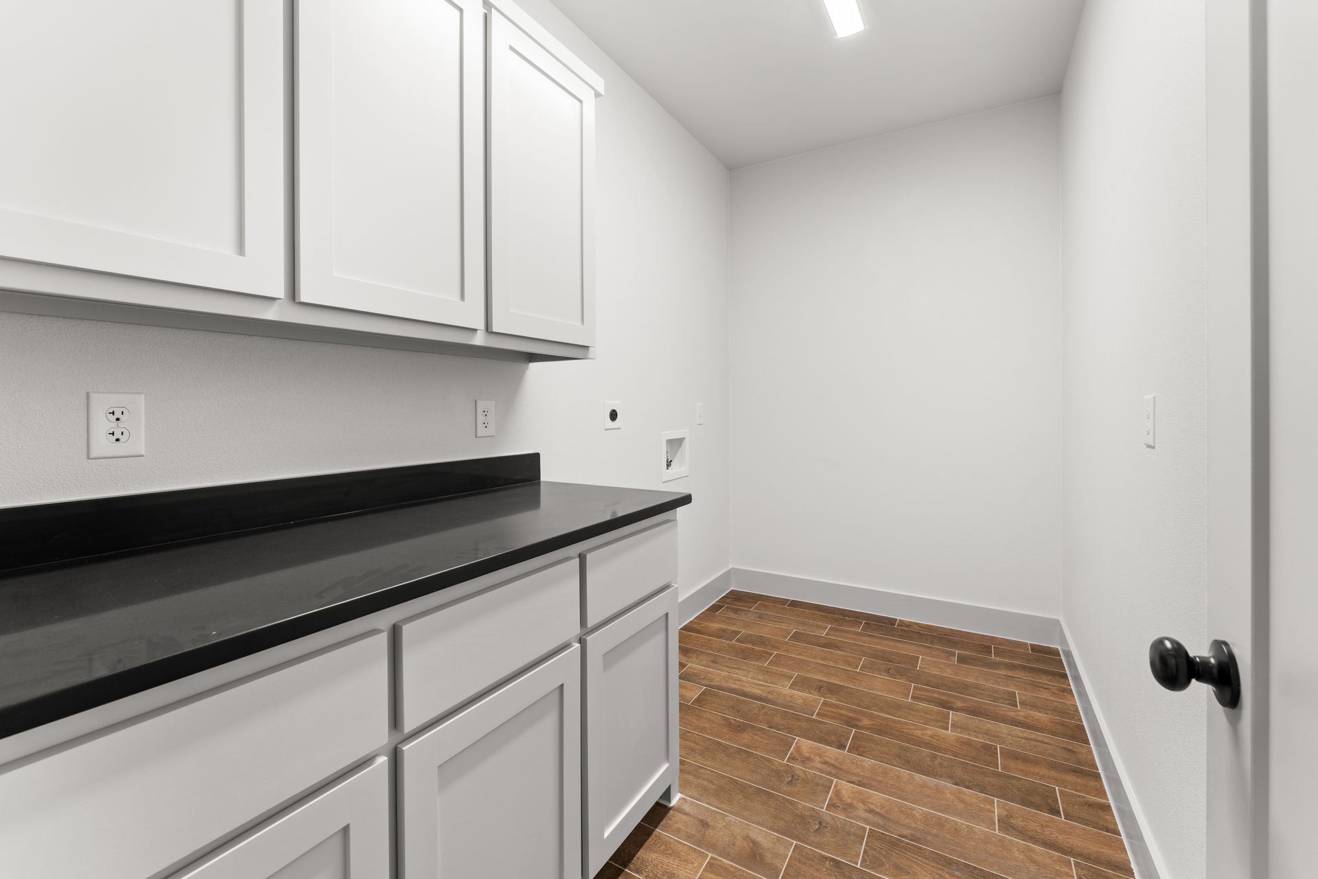 Laundry room with white cabinets, dark countertop, and wood floor.