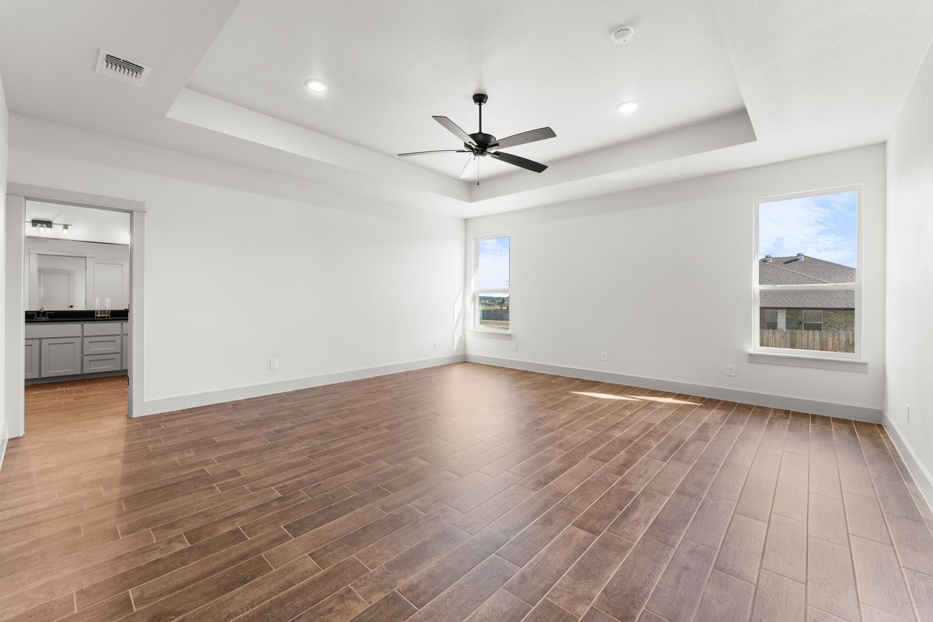 Empty, bright master bedroom with wood floors, white walls, and two windows.