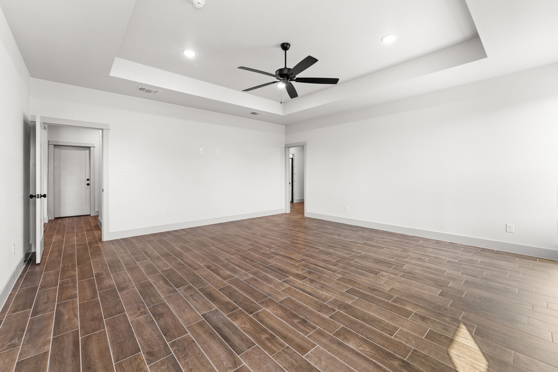 Empty room with hardwood floors, white walls, and a ceiling fan.