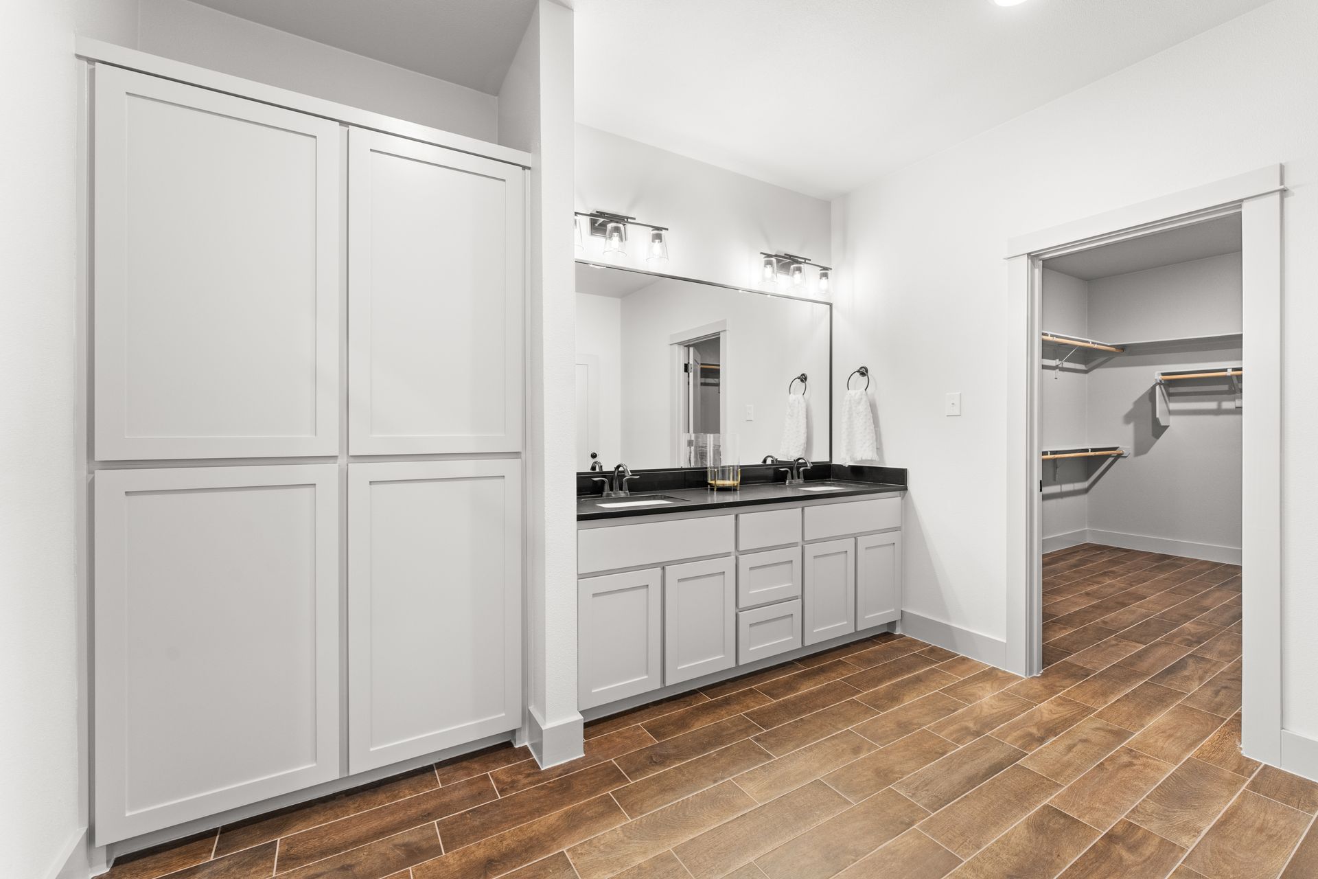 Bathroom with gray cabinets, double sink, and walk-in closet with wood floor.