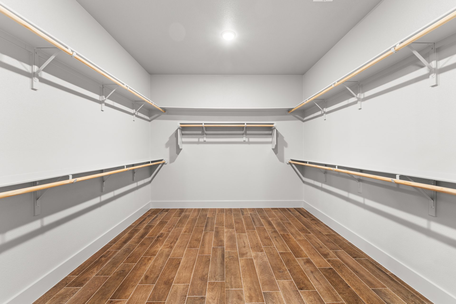 Empty walk-in closet with wooden floor, white walls, and built-in shelves.