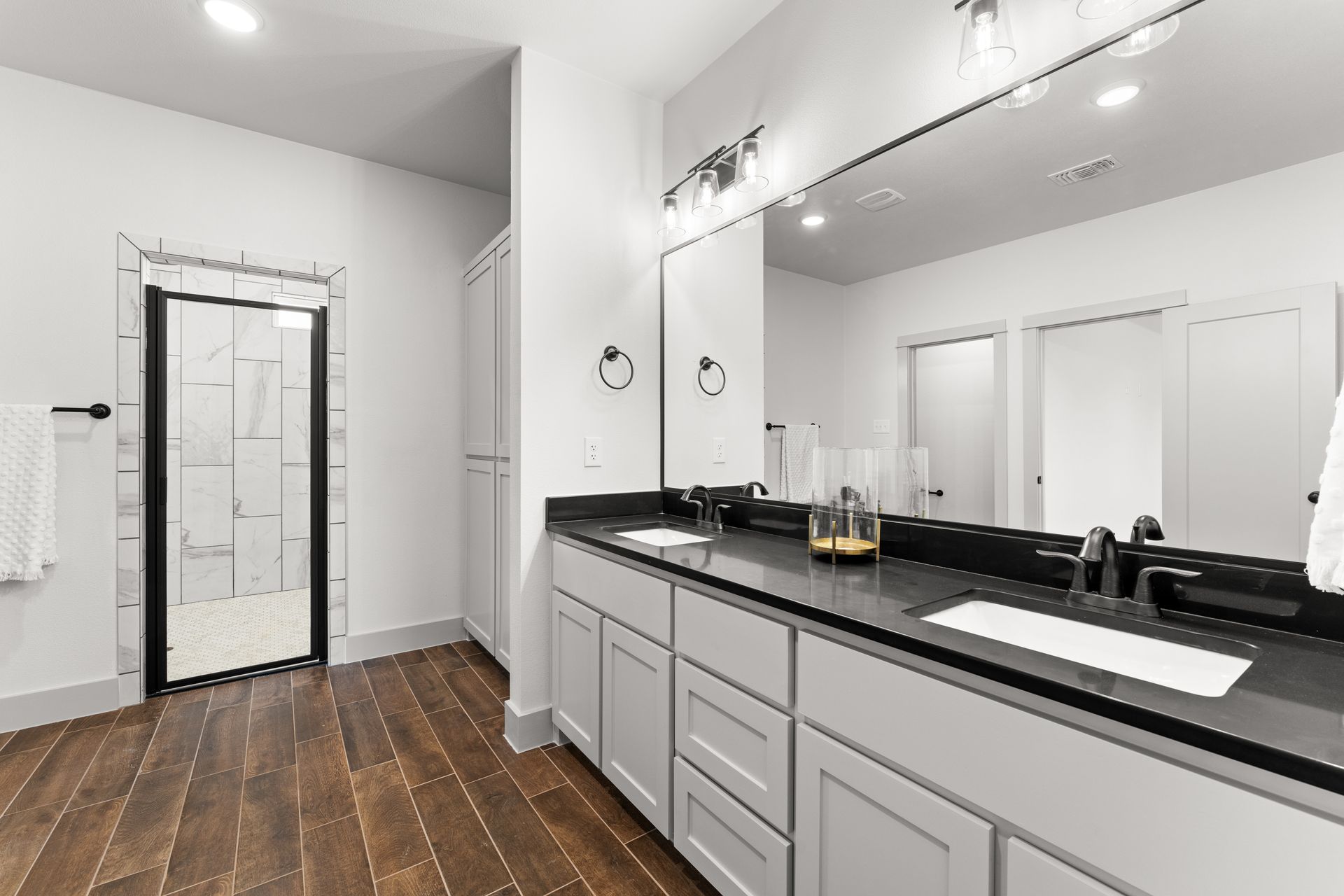 Modern bathroom with a double sink vanity, shower, and wood-look flooring.