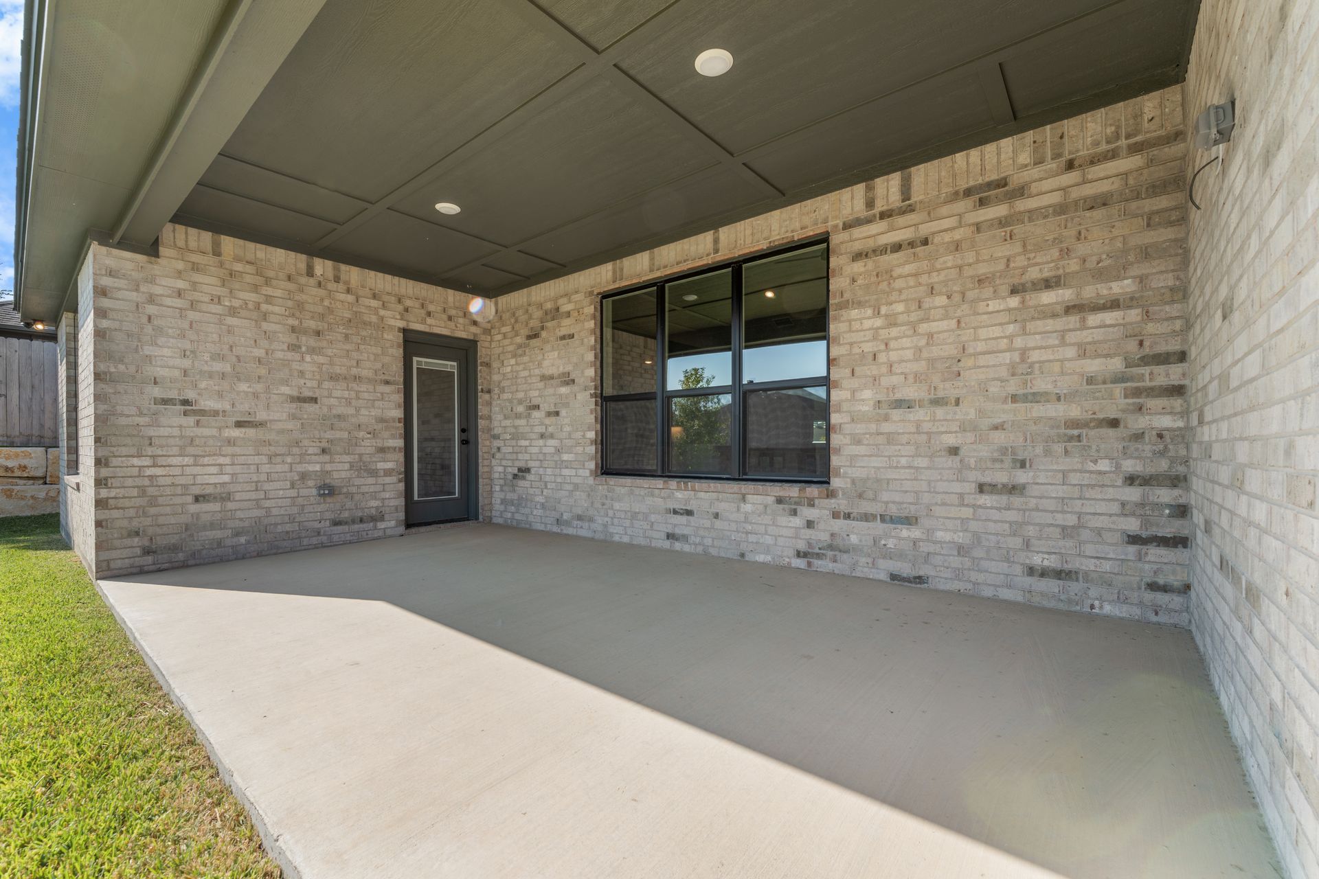 Covered outdoor patio with brick walls, concrete floor, and large window.