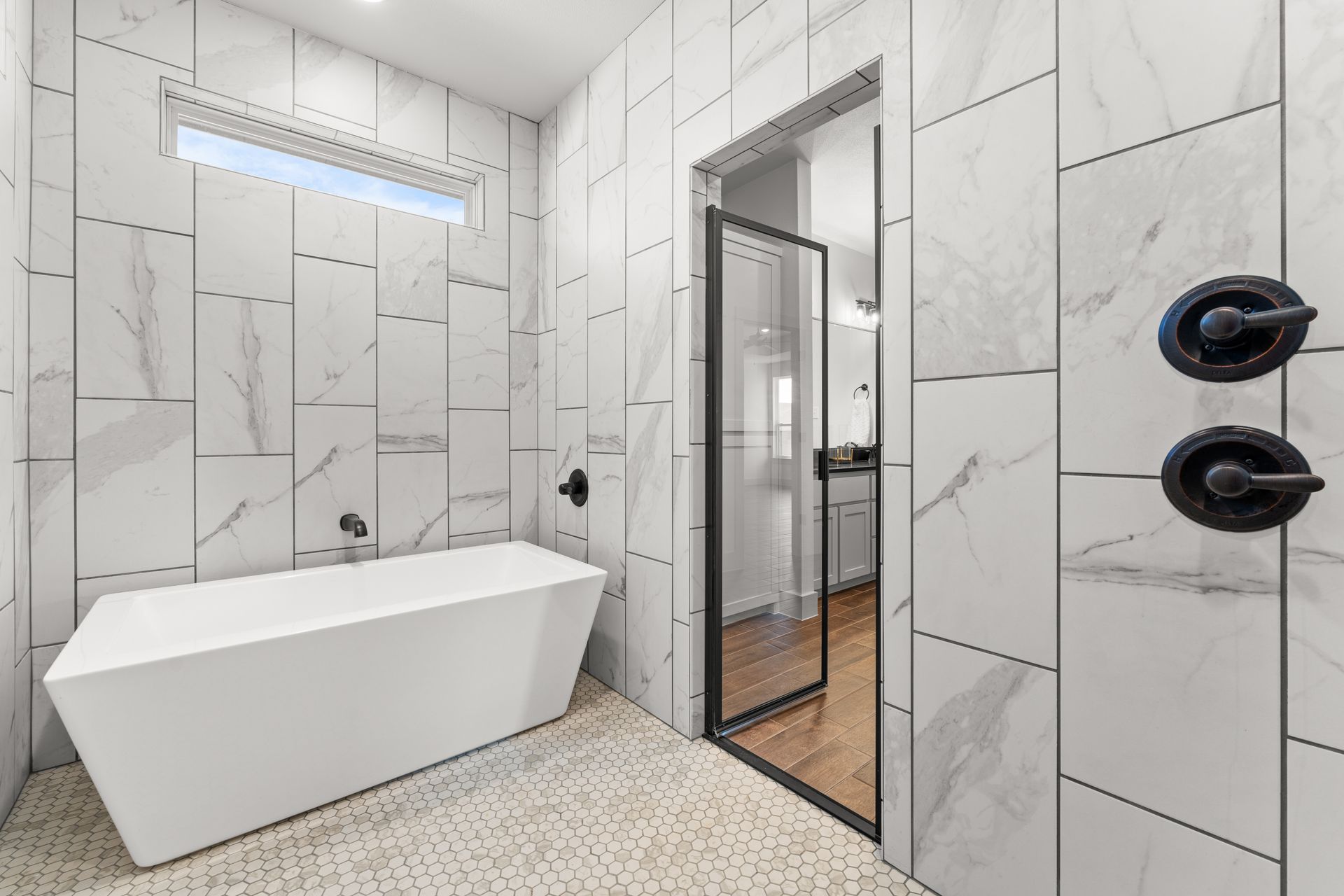 Modern bathroom with white marble tile, freestanding tub, and a shower with black hardware.